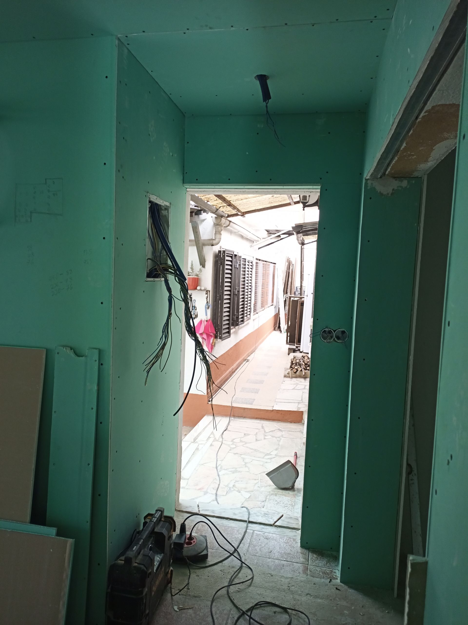 Corredor em construção, paredes pintadas de verde. Fiação elétrica exposta. Porta que dá para o exterior.