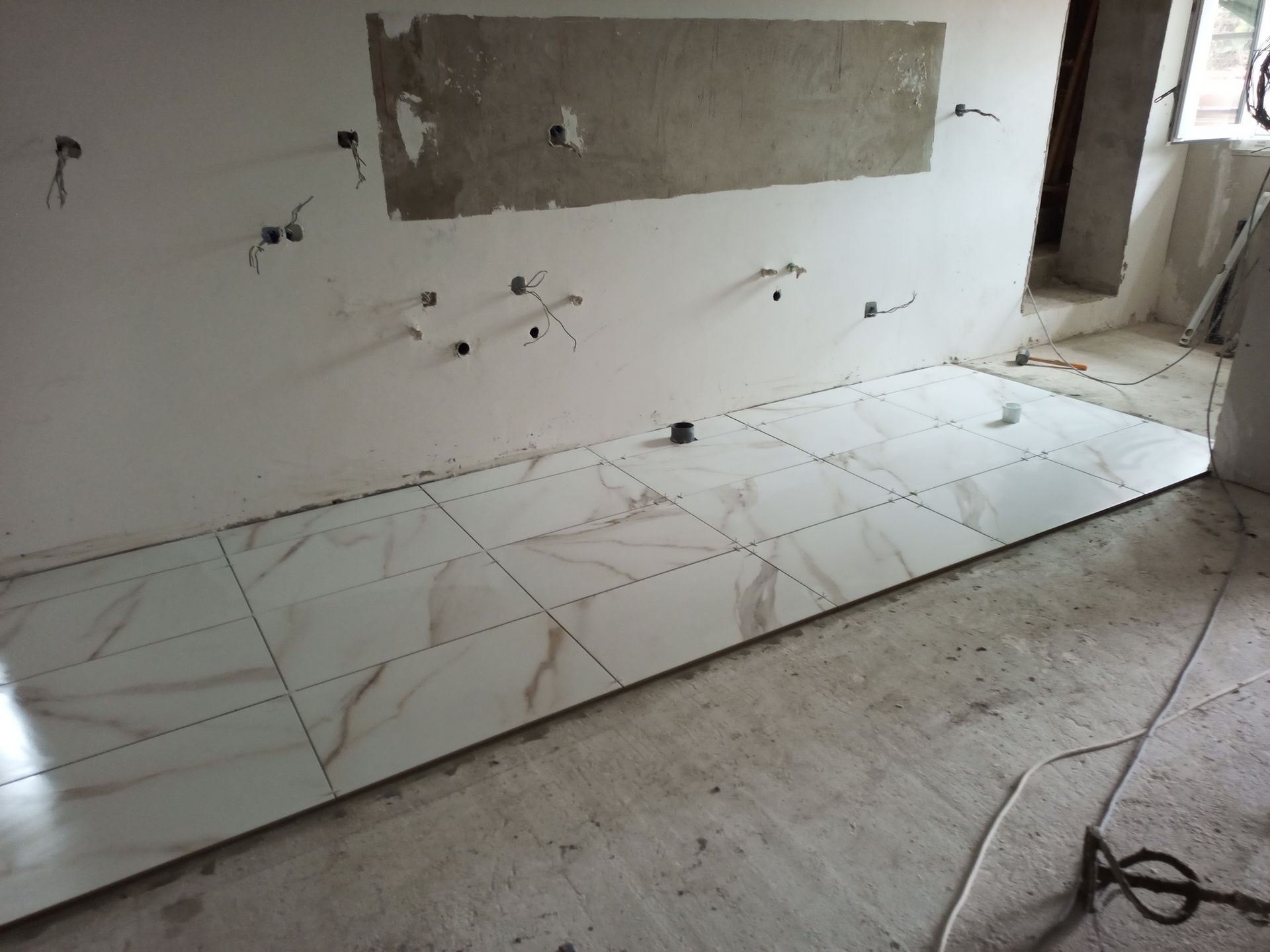 Interior em construção, com piso recém-instalado em imitação de mármore branco e marrom. Tomadas elétricas aparentes na parede.