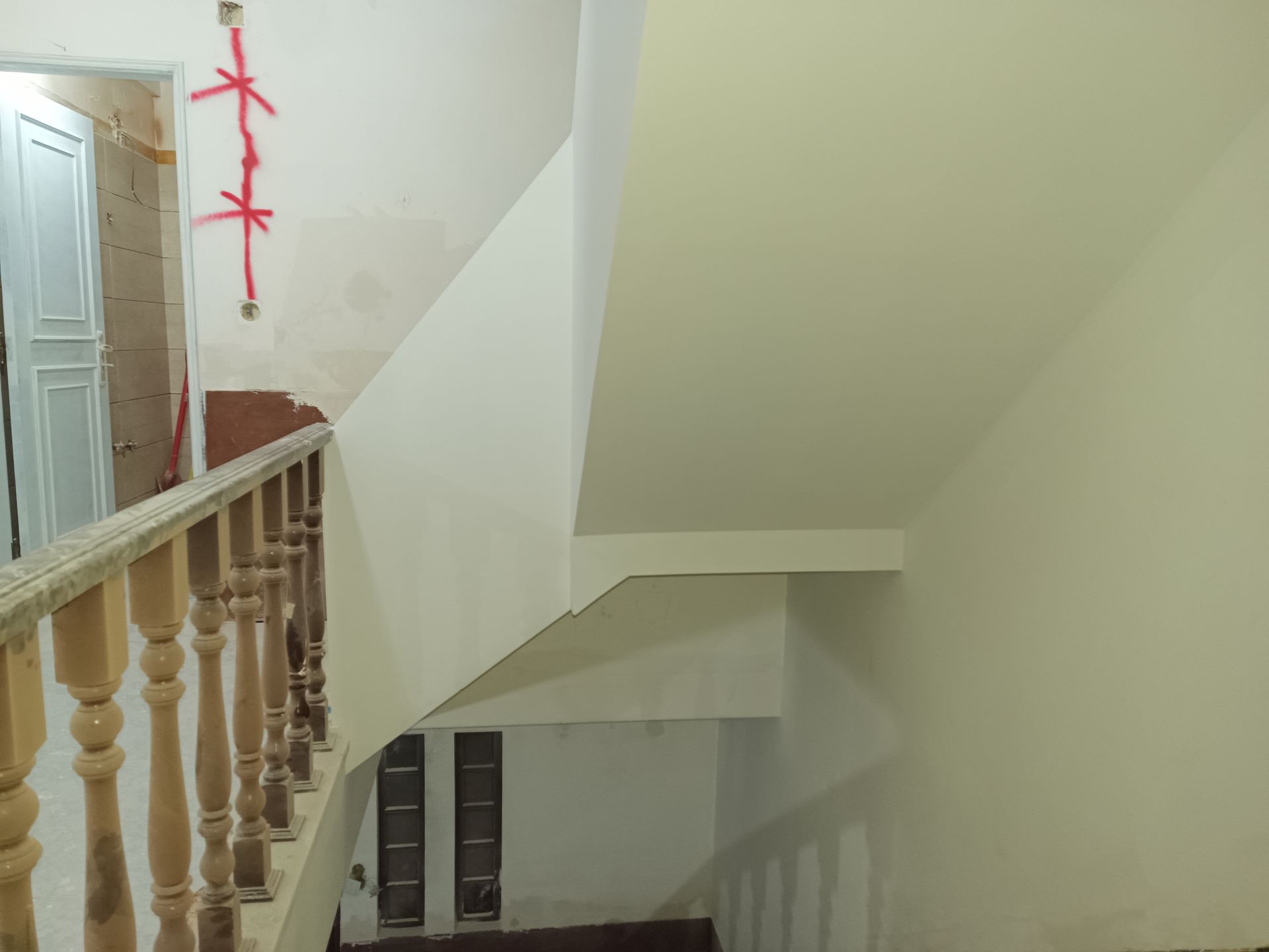 Escada com corrimão de madeira, paredes bege e fiação aparente contra uma parede branca perto de uma porta.