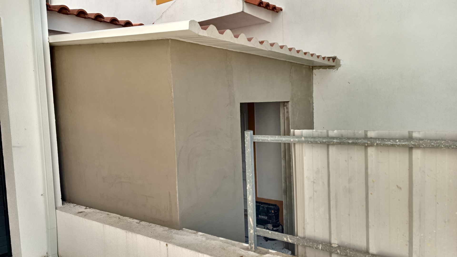 Um pequeno prédio de concreto bege com uma porta, ao lado de um portão de metal.