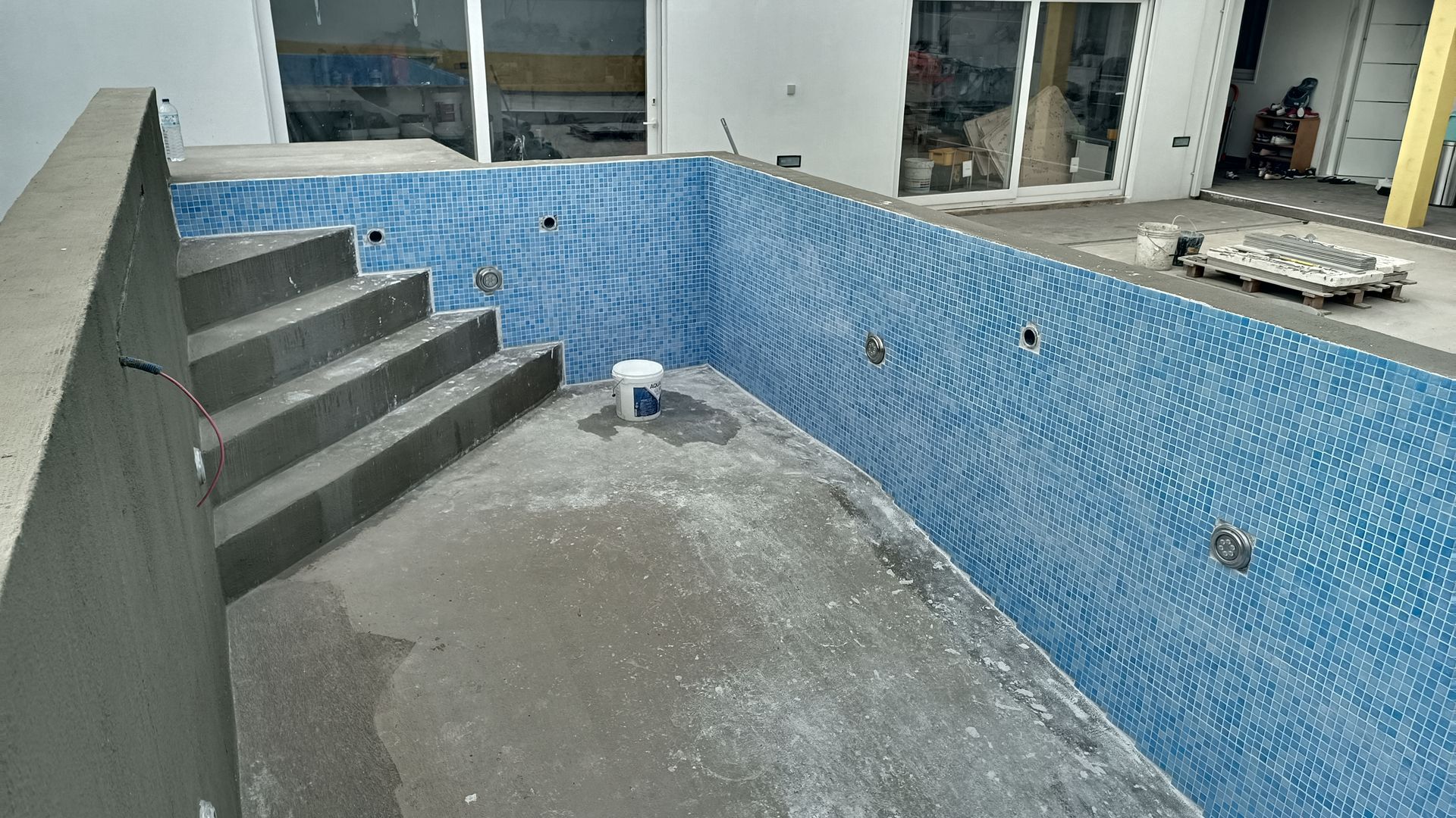 Piscina parcialmente construída com paredes revestidas de azulejos azuis e degraus de concreto.