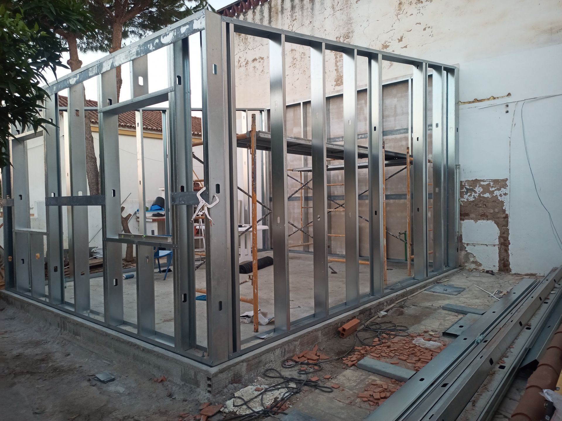 Estrutura metálica de um pequeno edifício em construção, contrastando com uma parede branca.