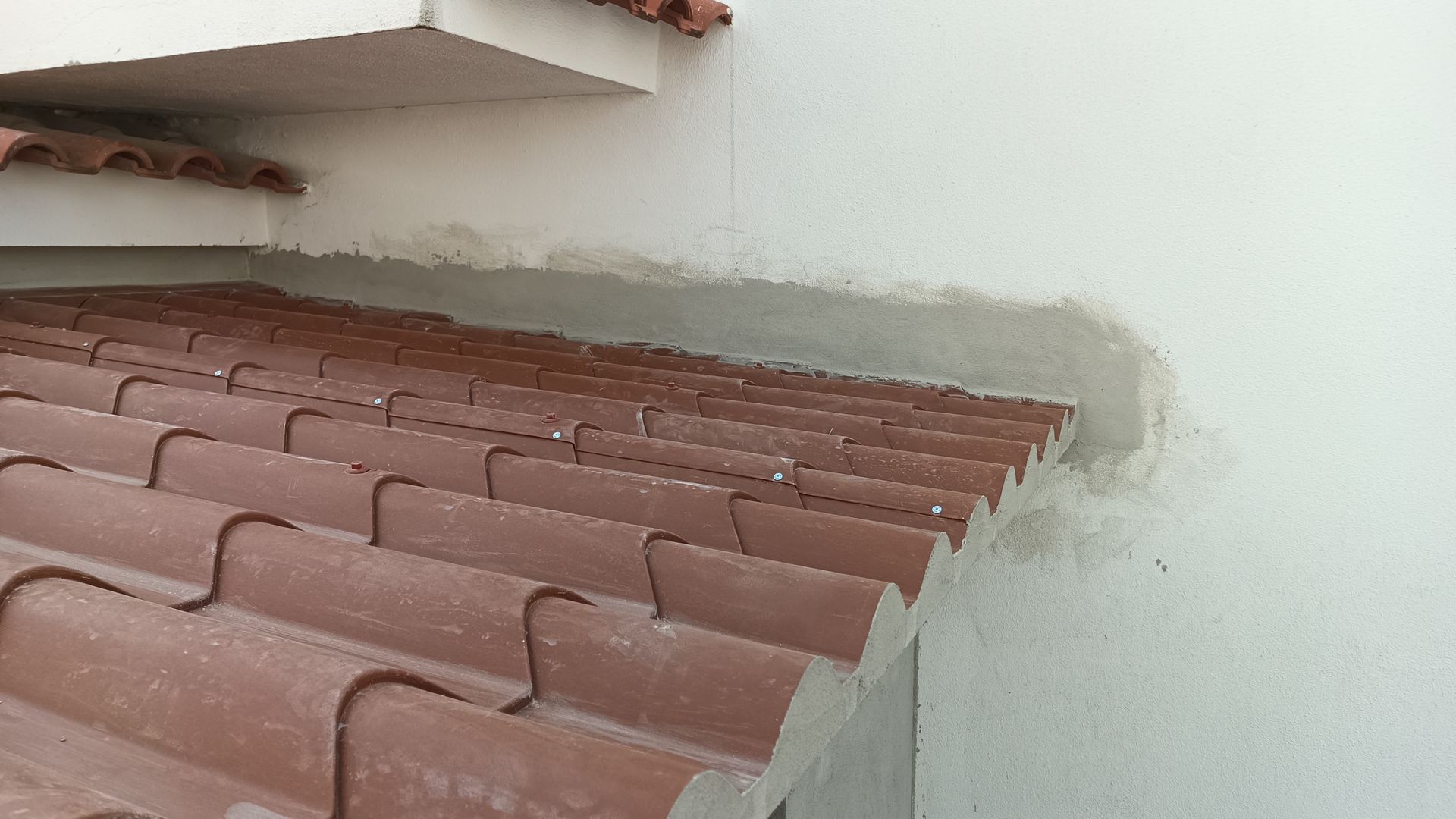 Telhas marrons encontram uma parede branca com selante cinza.