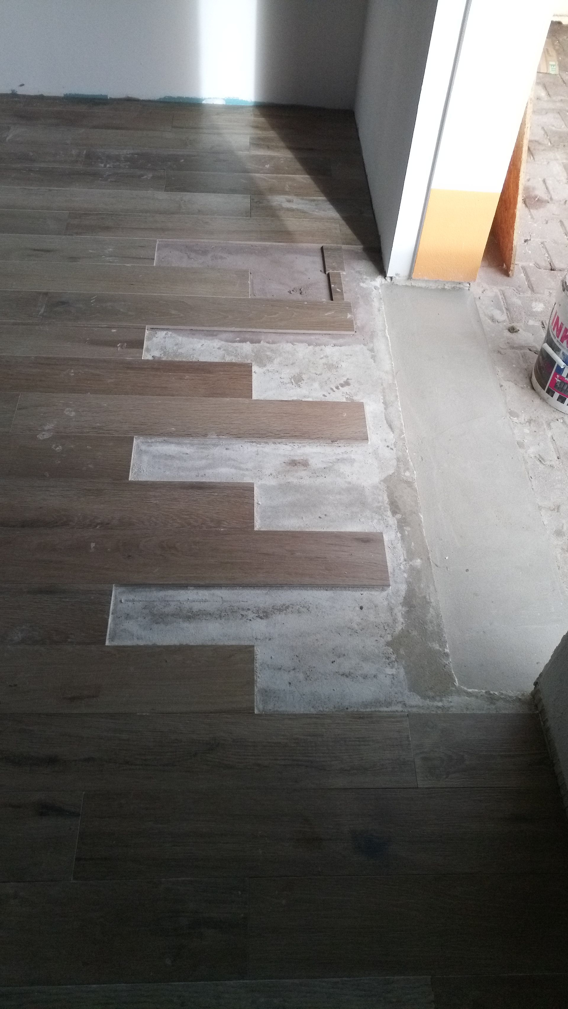 Piso de madeira com partes faltantes, adjacente a uma porta de concreto.