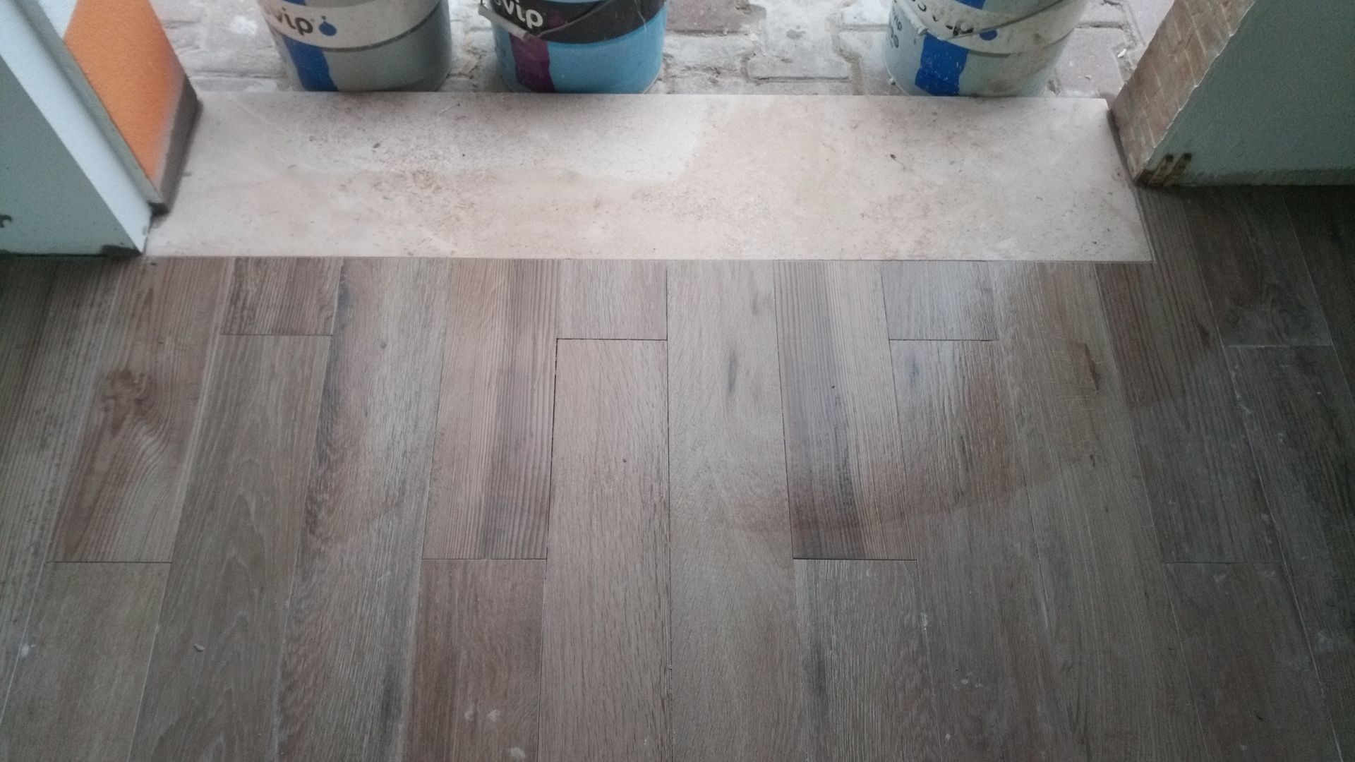 Piso imitando madeira com rejunte bege claro. Proteção de papel na entrada com baldes atrás.