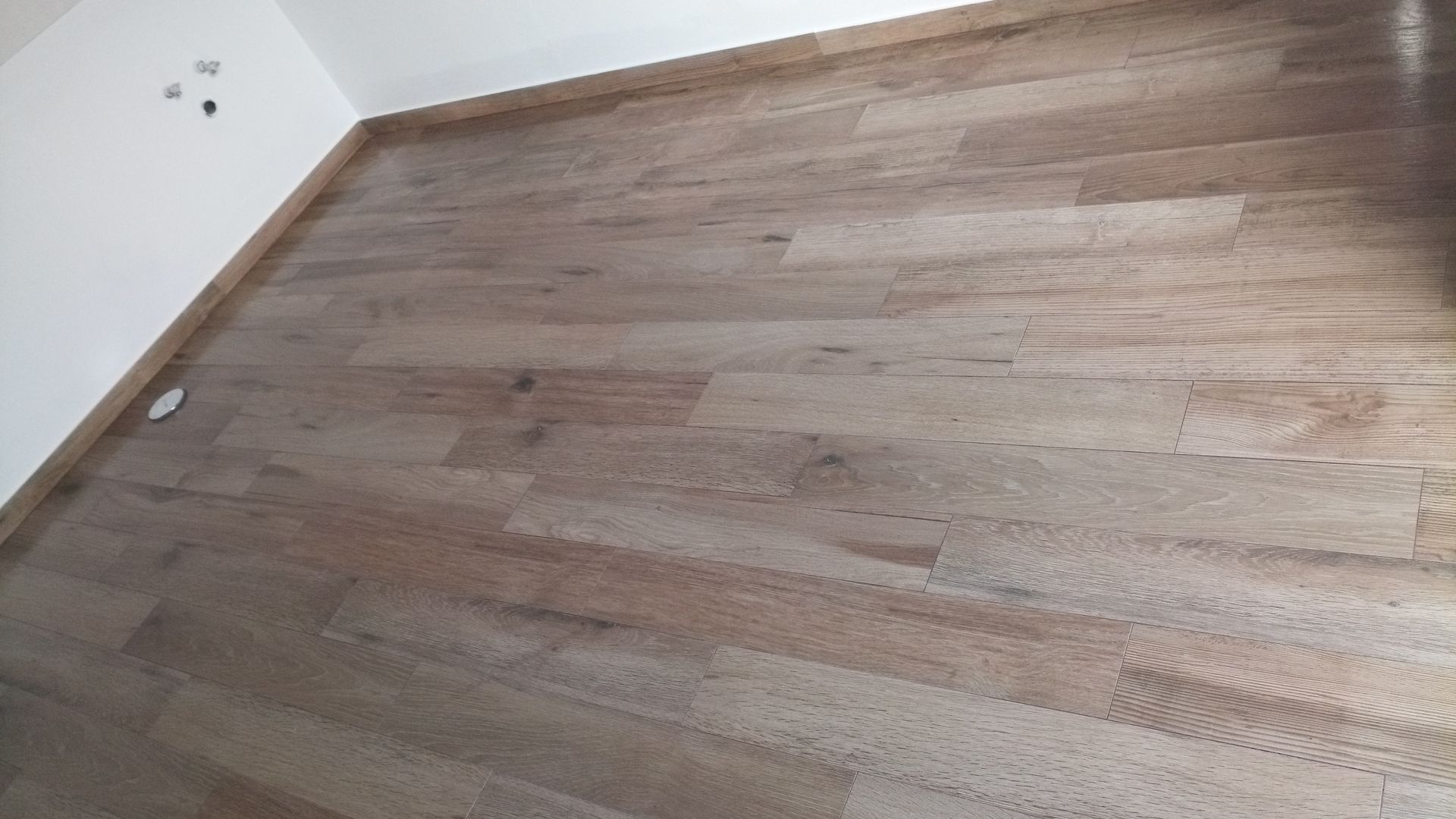 Piso de madeira, castanho claro com veios discretos, em uma sala com paredes brancas e uma faixa decorativa também castanha clara.