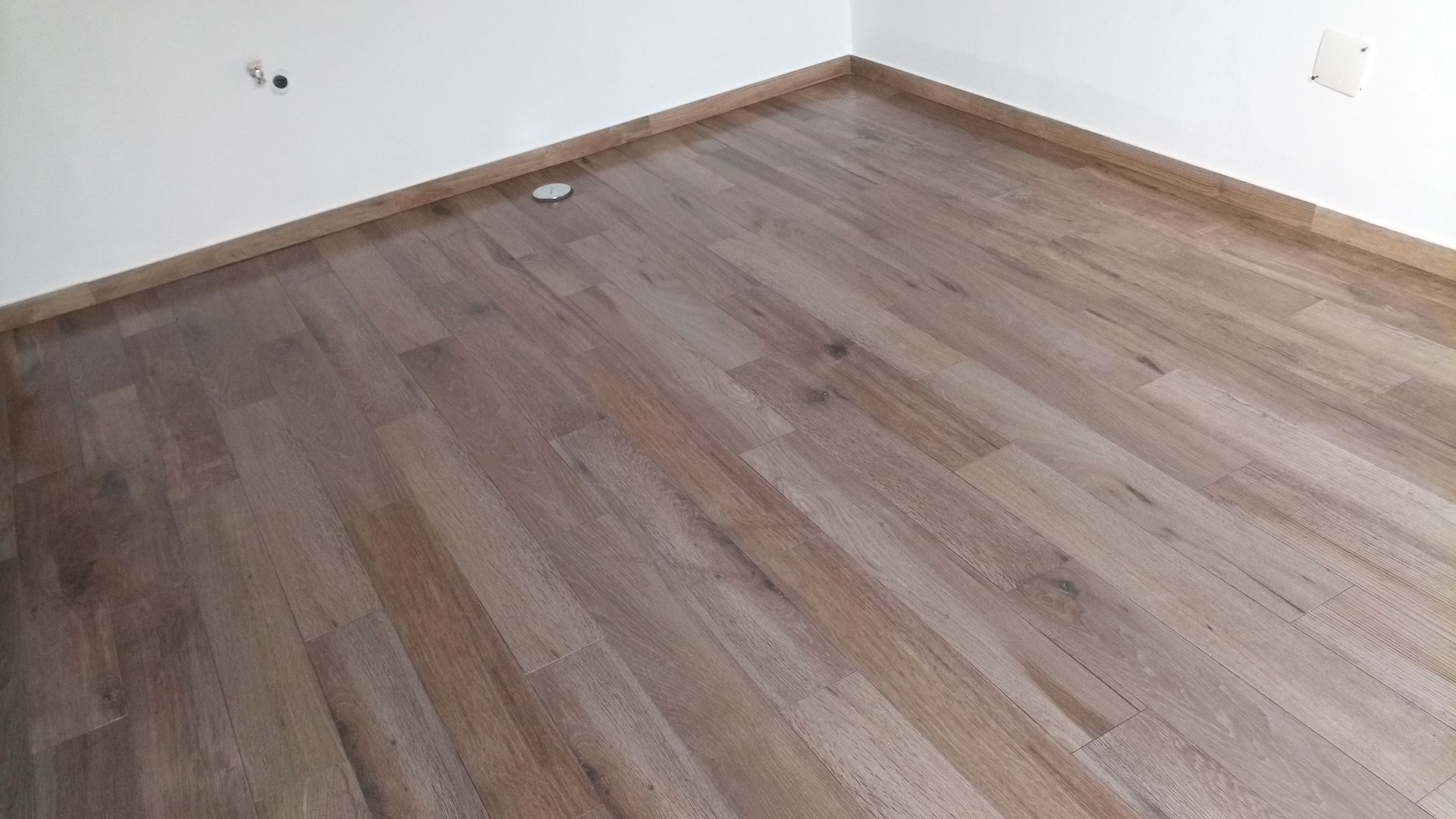 Piso de madeira com rodapés ao longo das paredes brancas de um quarto.