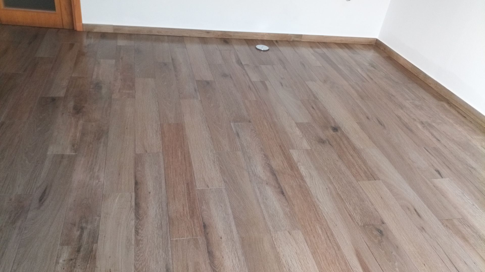 Piso de madeira maciça em um cômodo com paredes brancas e batente de porta de madeira.