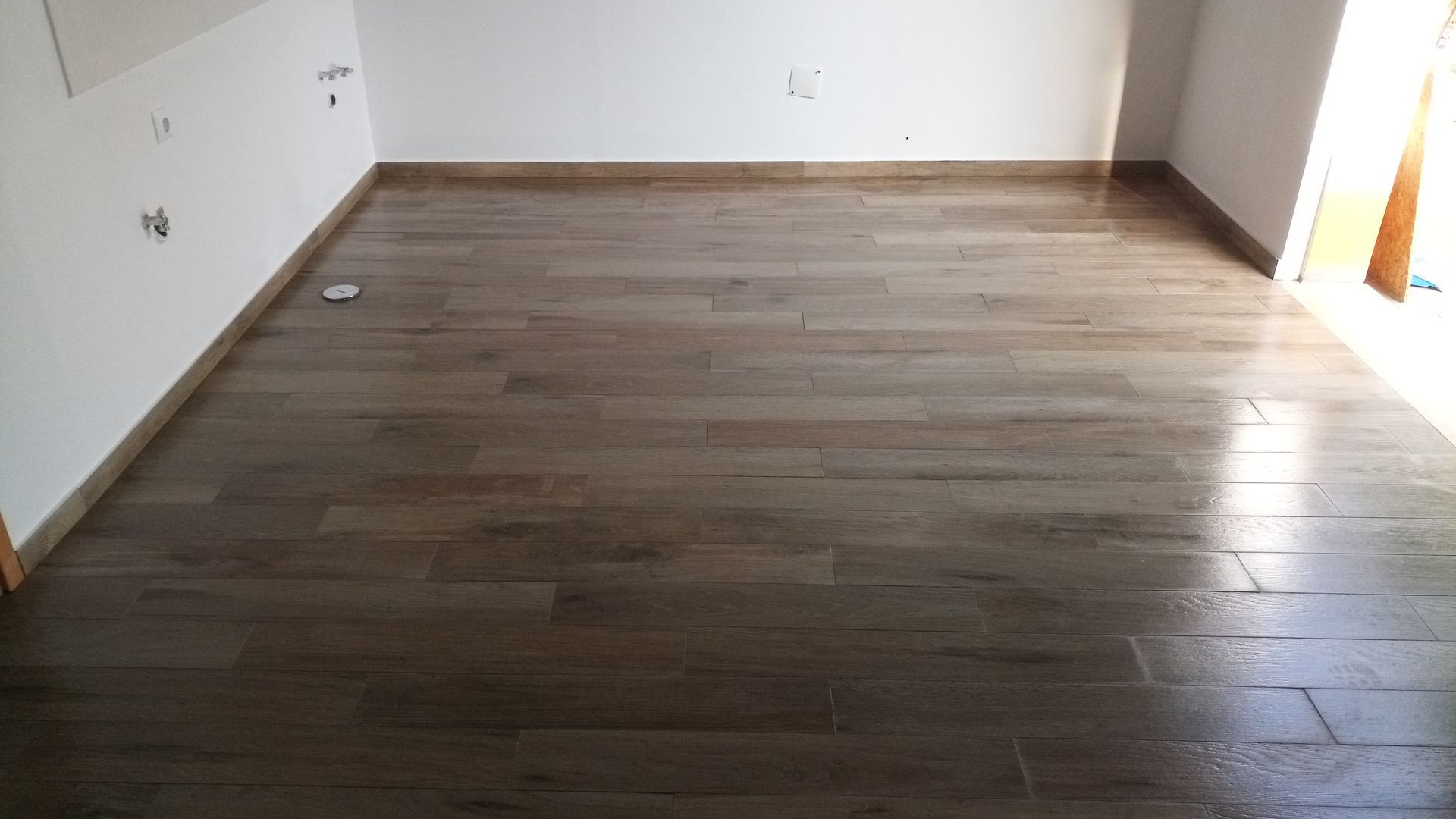 Piso de madeira em um cômodo vazio com paredes brancas e luz natural.