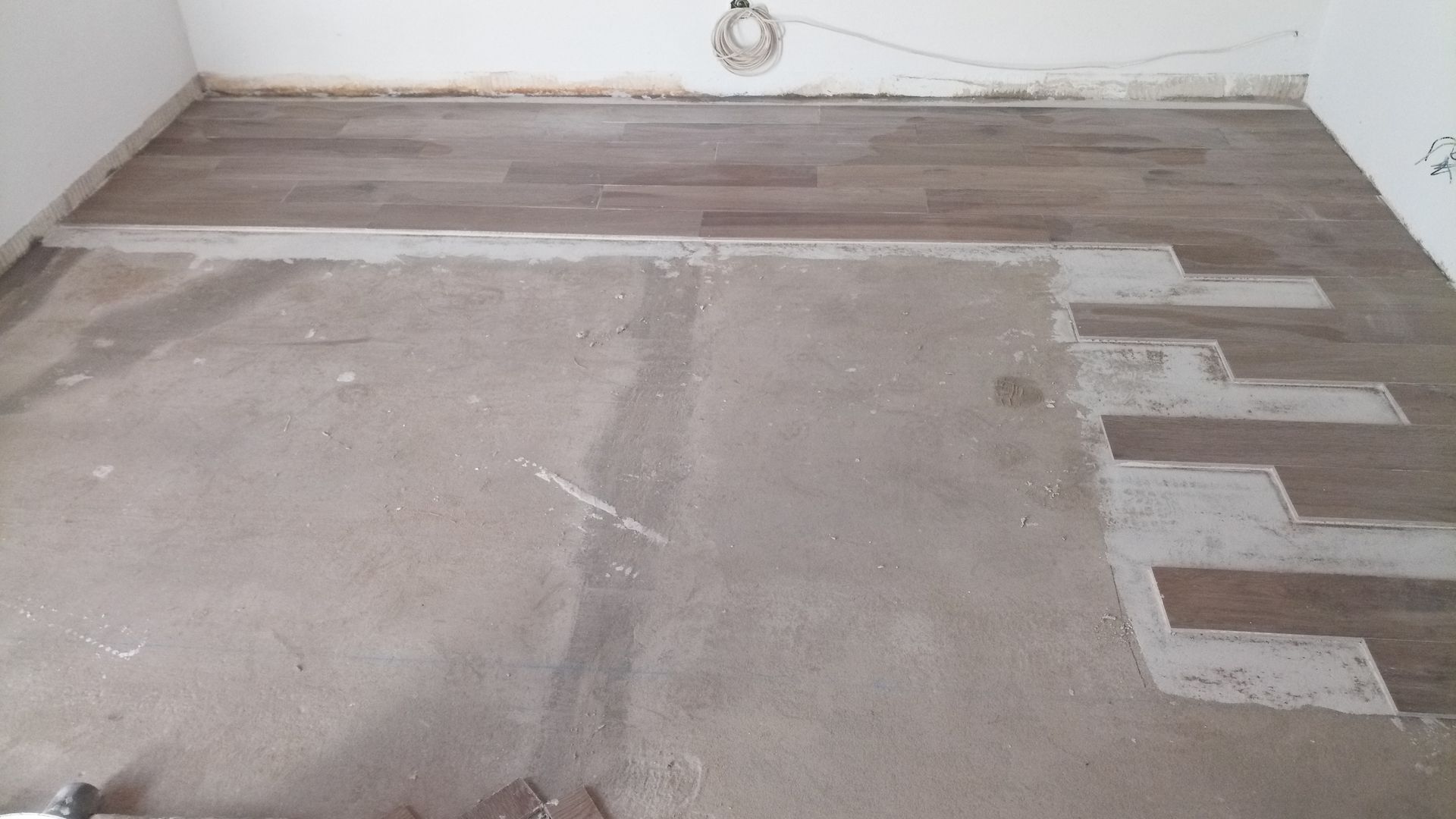 Sala com piso de madeira parcialmente instalado sobre contrapiso de concreto. As tábuas marrom-claras são assentadas em seções.
