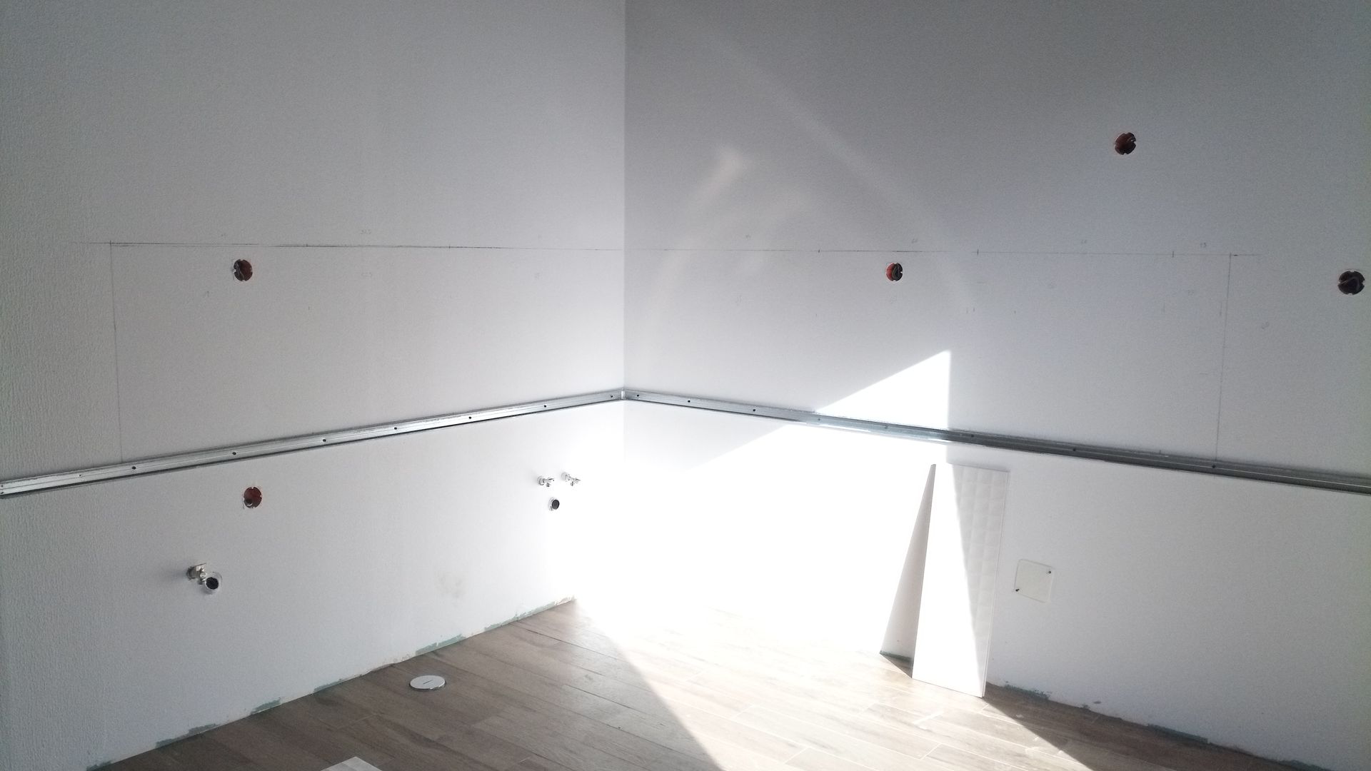 Canto interno de um cômodo em construção com drywall e caixas elétricas expostas. A luz do sol entra abundantemente.