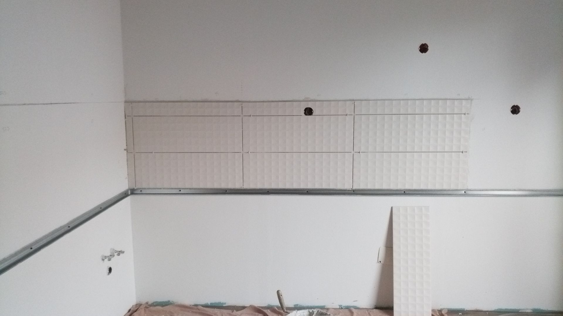 Parede interna com grades metálicas, painel de azulejos parcialmente revestido e tomadas elétricas.