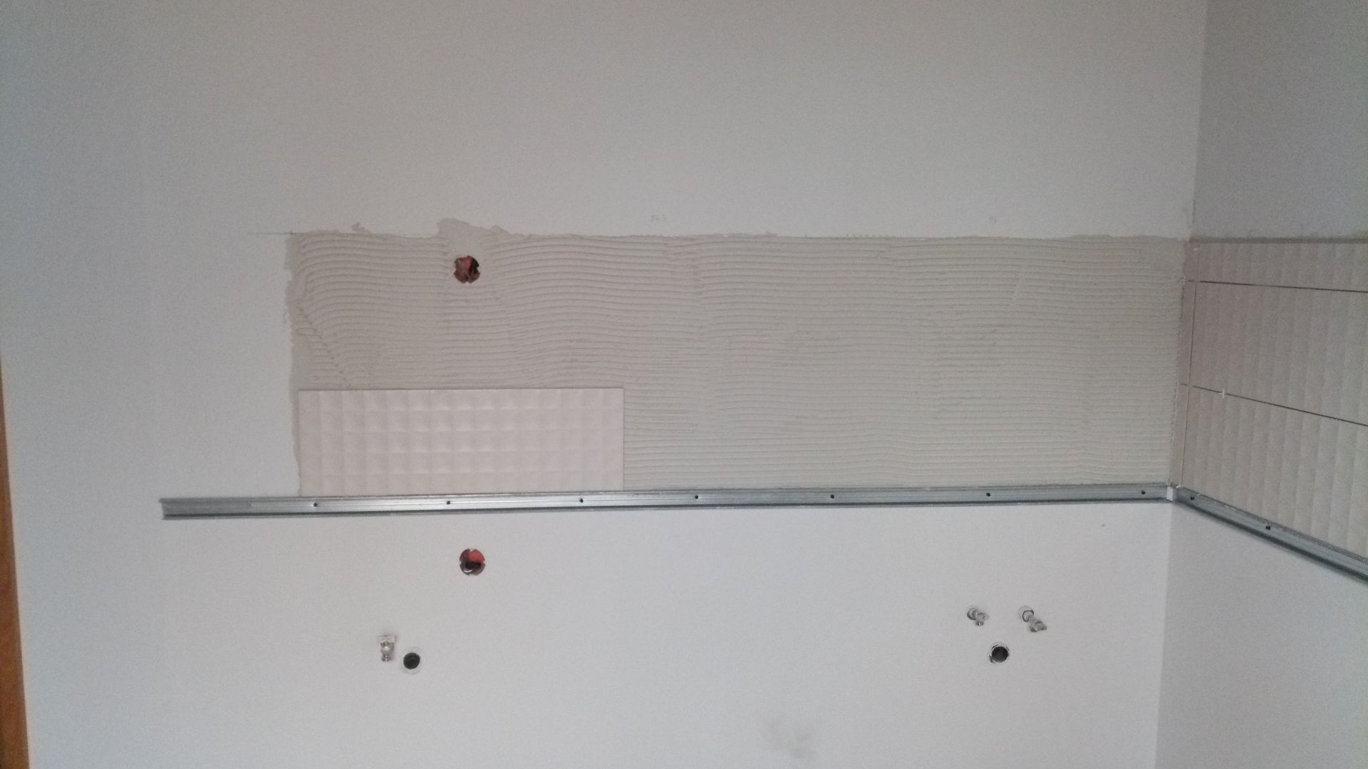 Parede com suporte para prateleira, drywall e área parcialmente revestida com azulejos; furos para acessórios visíveis.