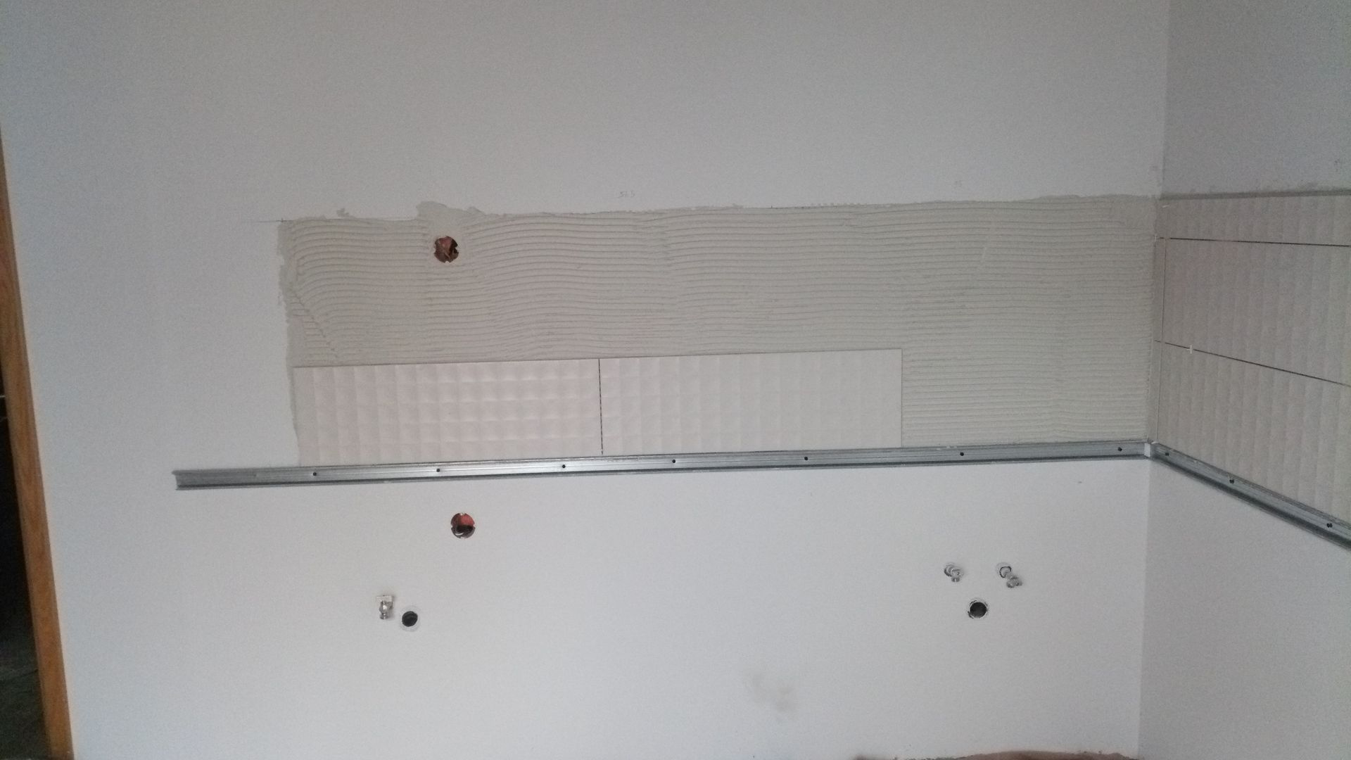 Parede da cozinha com azulejos parcialmente instalados e moldura metálica.
