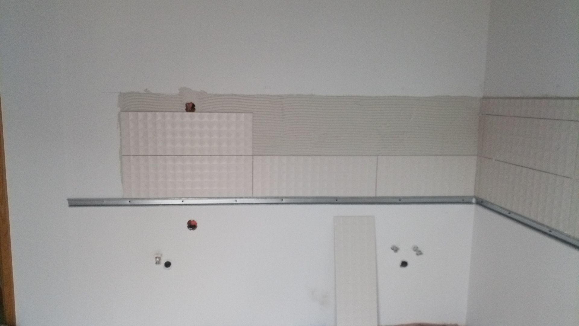 Parede branca com revestimento parcial de azulejos e faixa de suporte metálica.