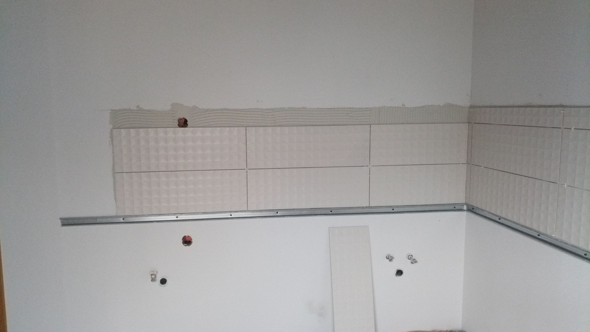Parede da cozinha com azulejos brancos parcialmente instalados e acabamento metálico.