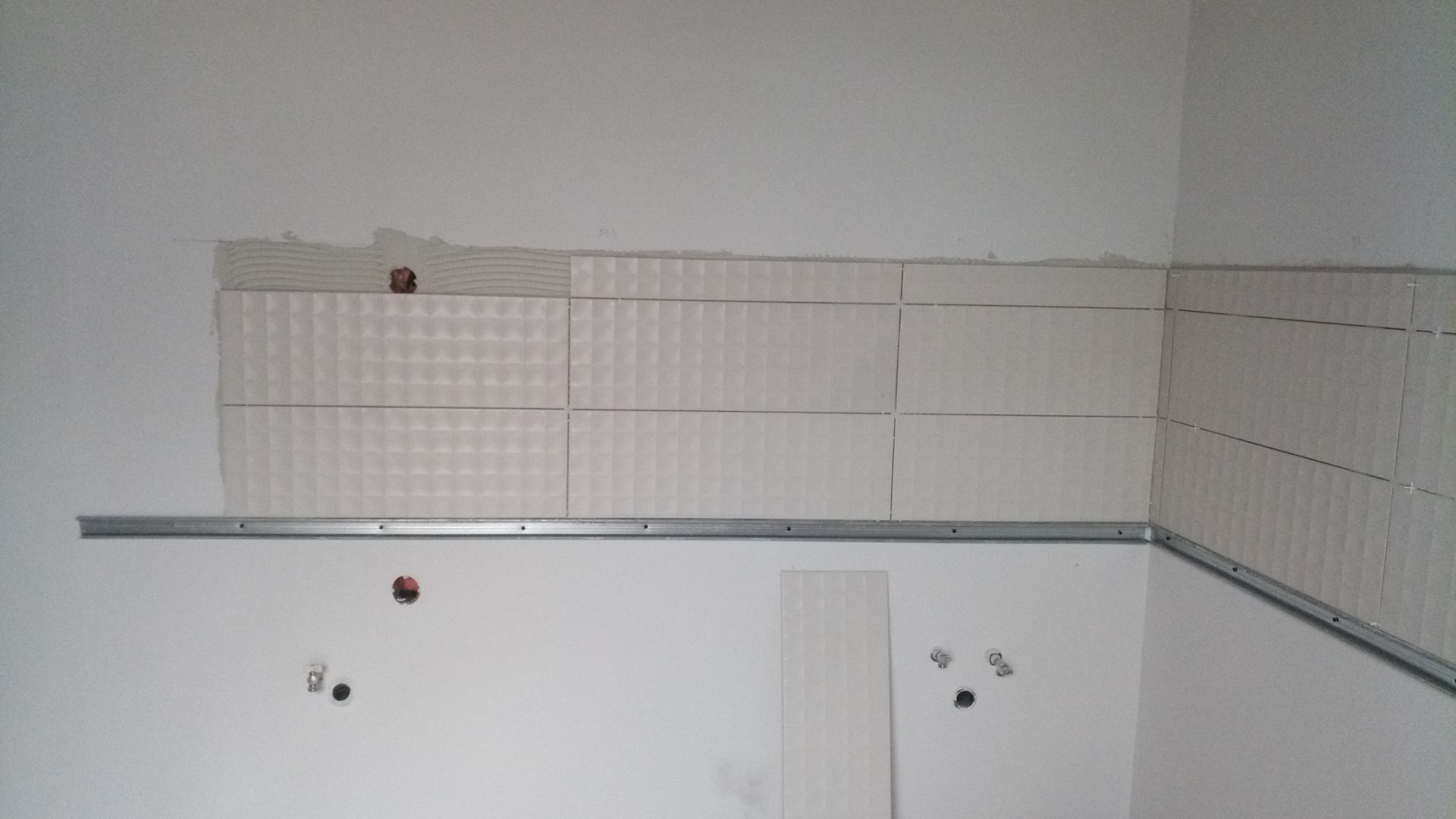Azulejos brancos sendo instalados em uma parede branca; uma barra de suporte de metal está fixada.