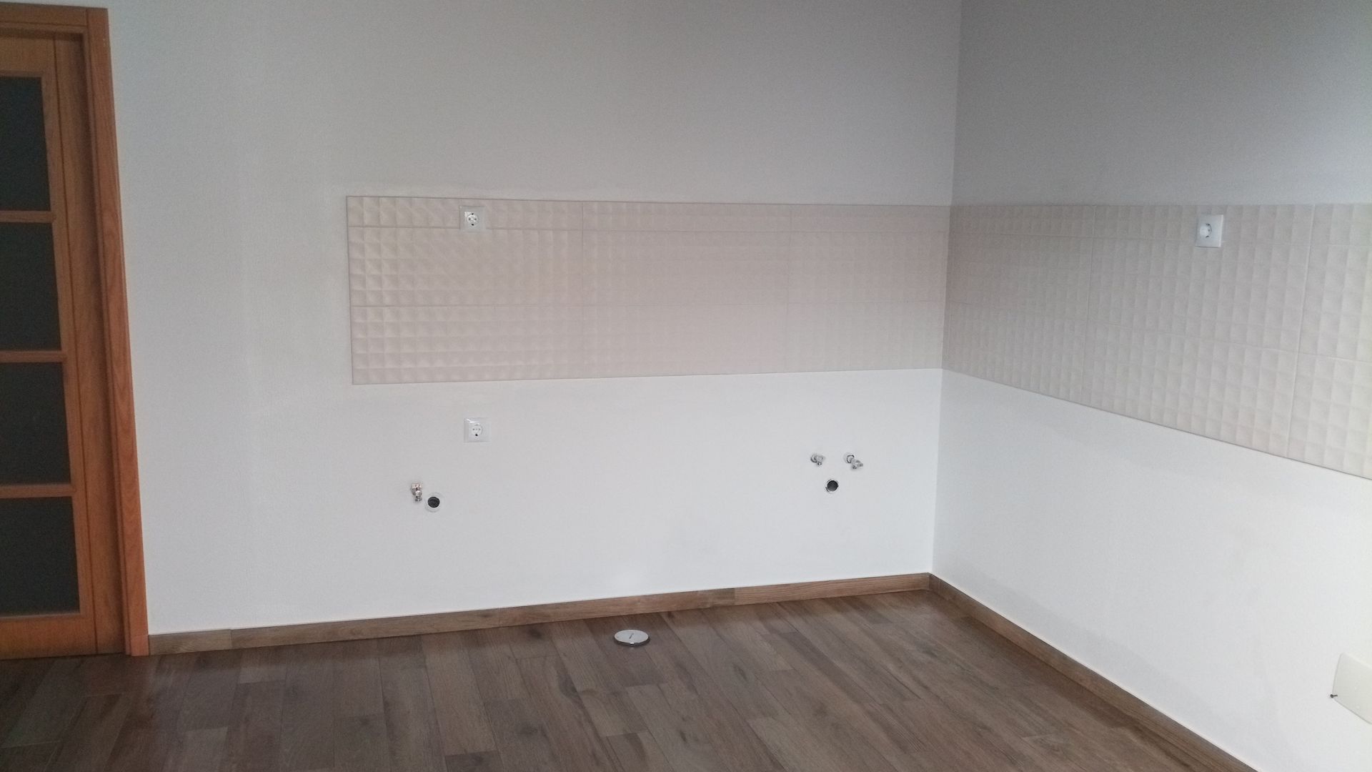 Quarto vazio com paredes brancas, piso de madeira e uma porta à esquerda.