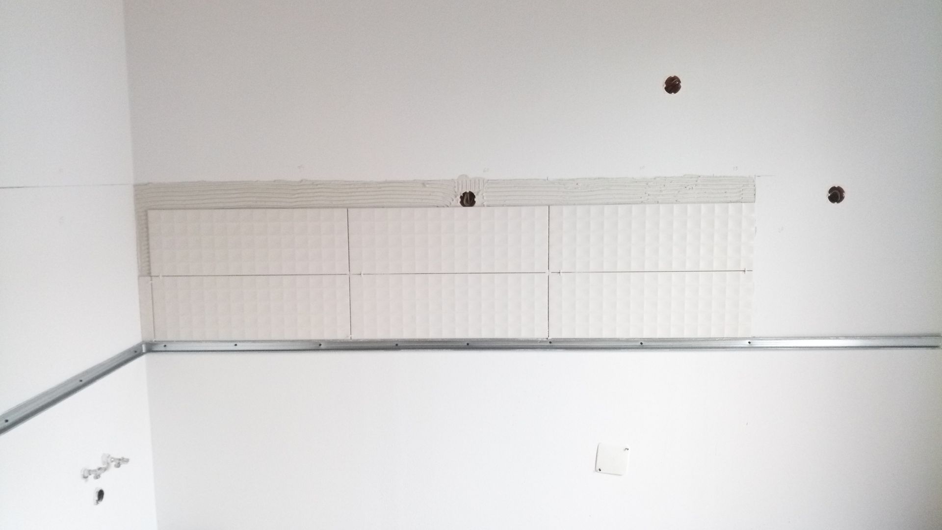 Parede branca em construção com estrutura metálica e seção retangular rebaixada.