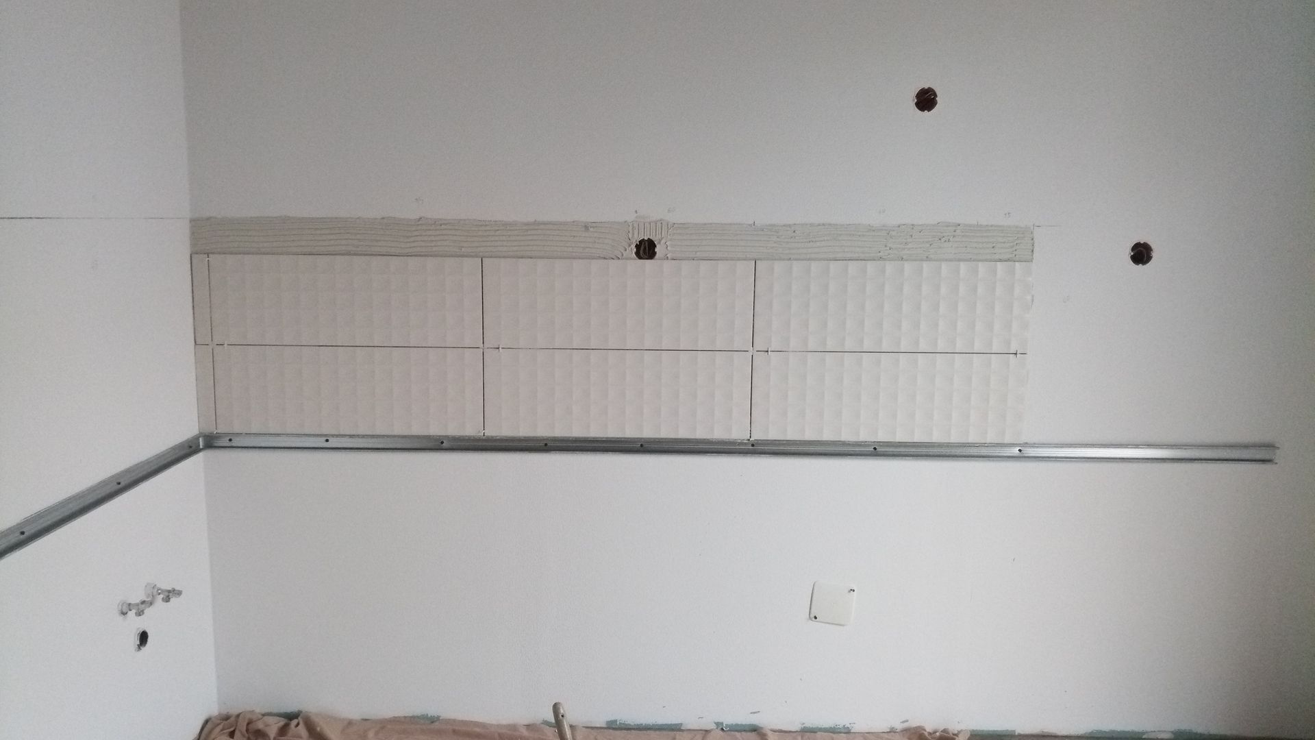 Parede interna com estrutura metálica aparente, drywall e superfície parcialmente revestida com azulejos. Tomadas elétricas presentes.