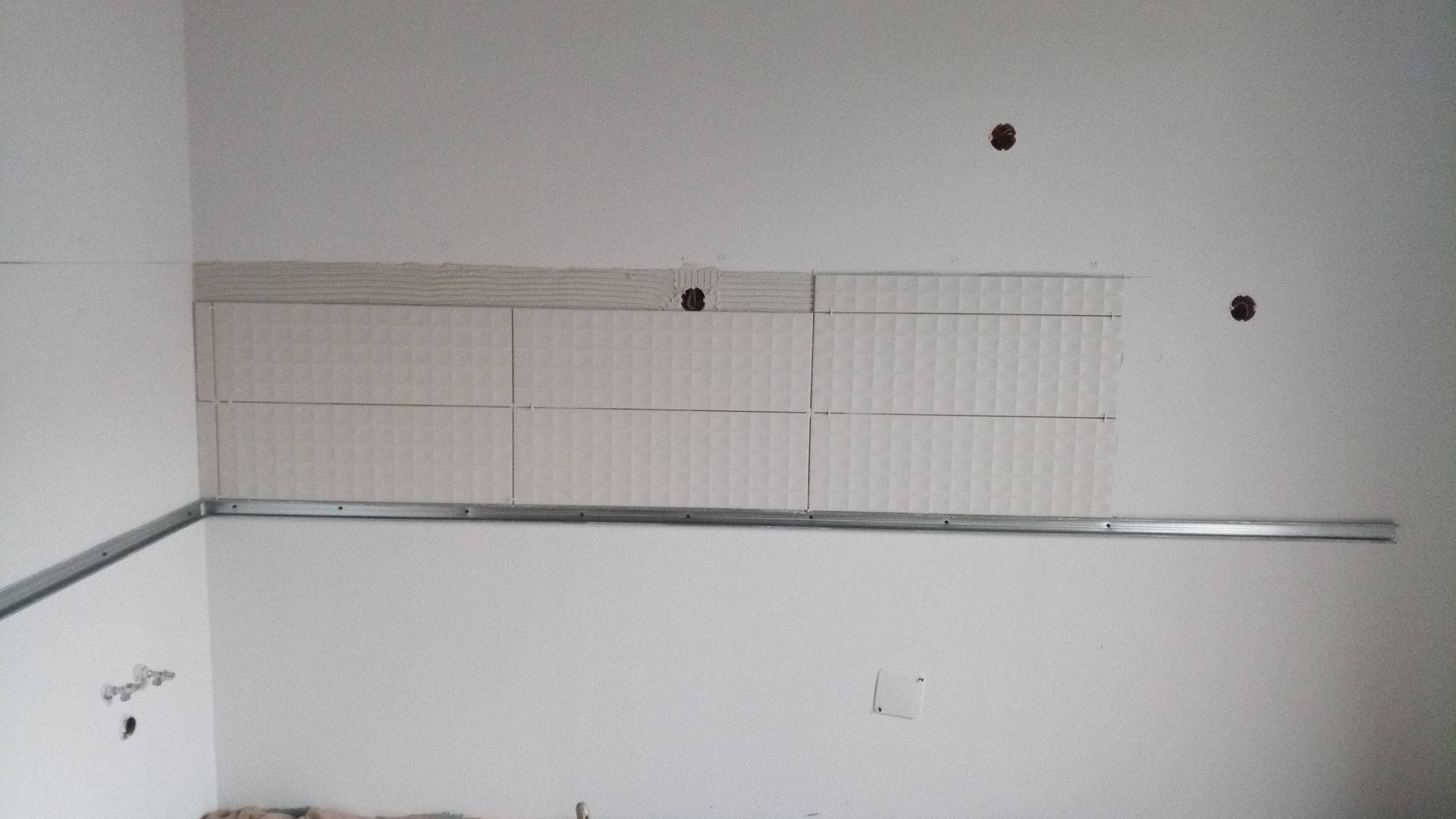 Parede interna com estrutura metálica para prateleiras embutidas, sem acabamento e com furos para instalação elétrica.