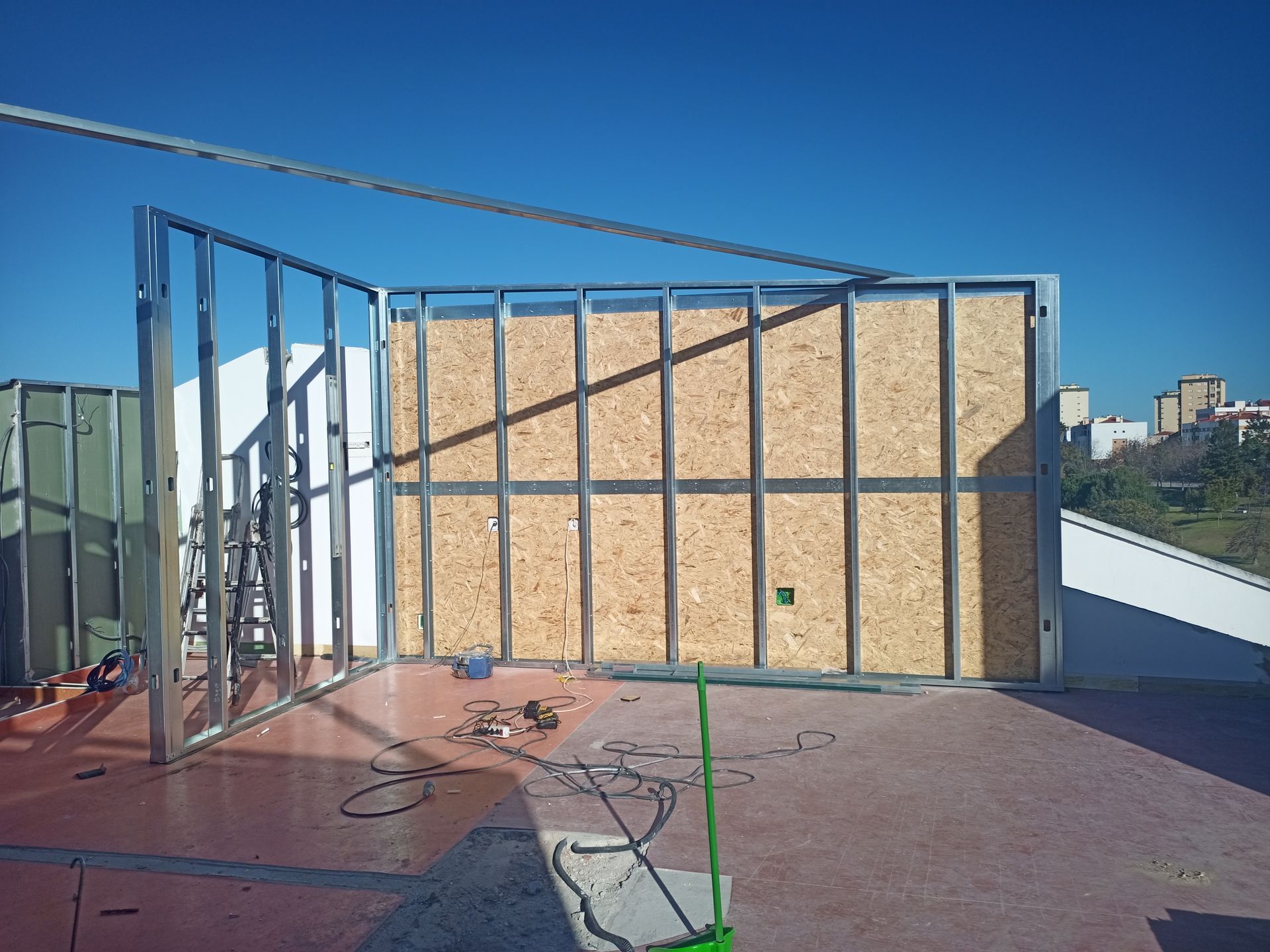 Estrutura de aço de uma parede com painéis de madeira em um telhado sob um céu azul.