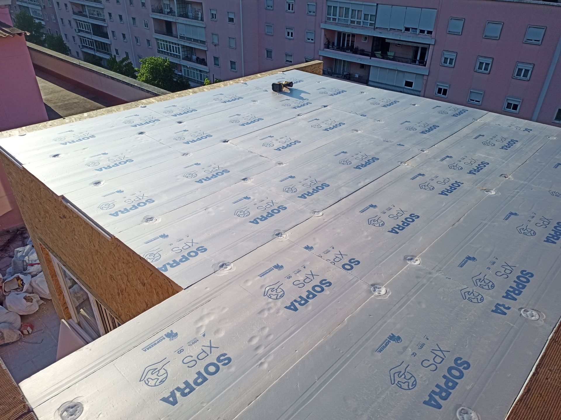 Telhado com material isolante prateado, provavelmente para impermeabilização. Construção civil, dia ensolarado.