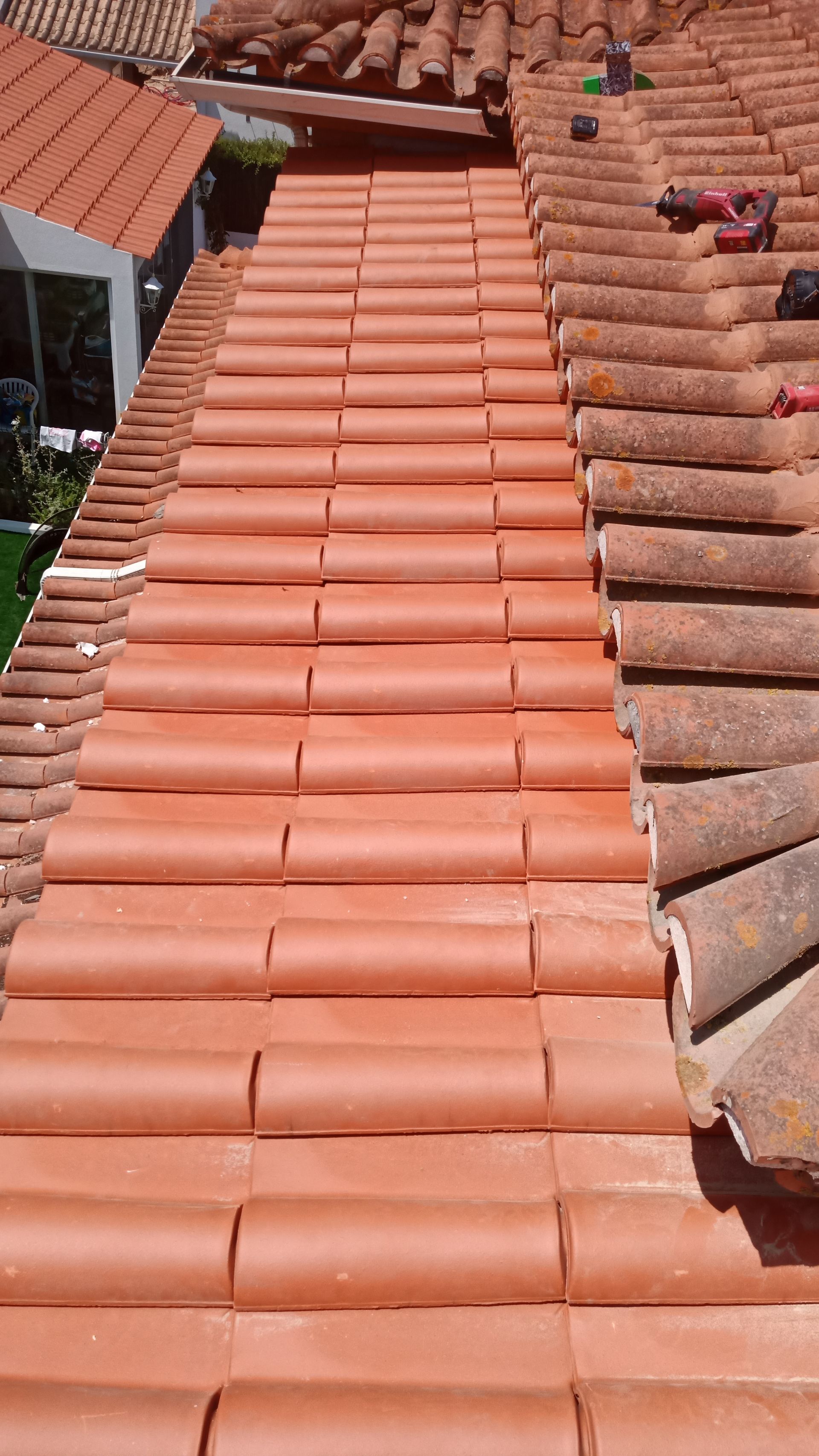 Telhado de telha de barro vermelha com uma seção central; luz solar.