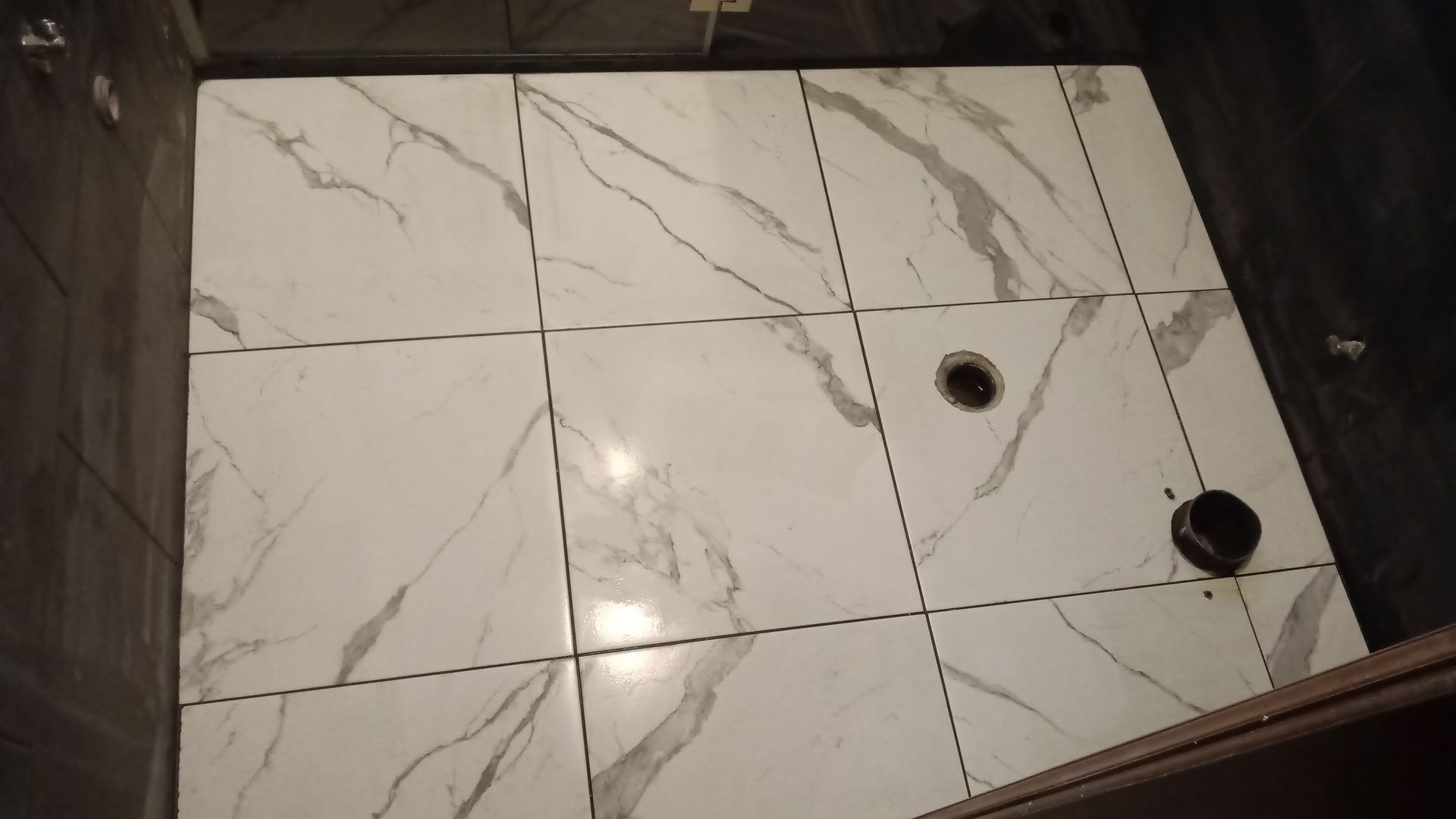 Piso do chuveiro com azulejos brancos imitando mármore e ralo.