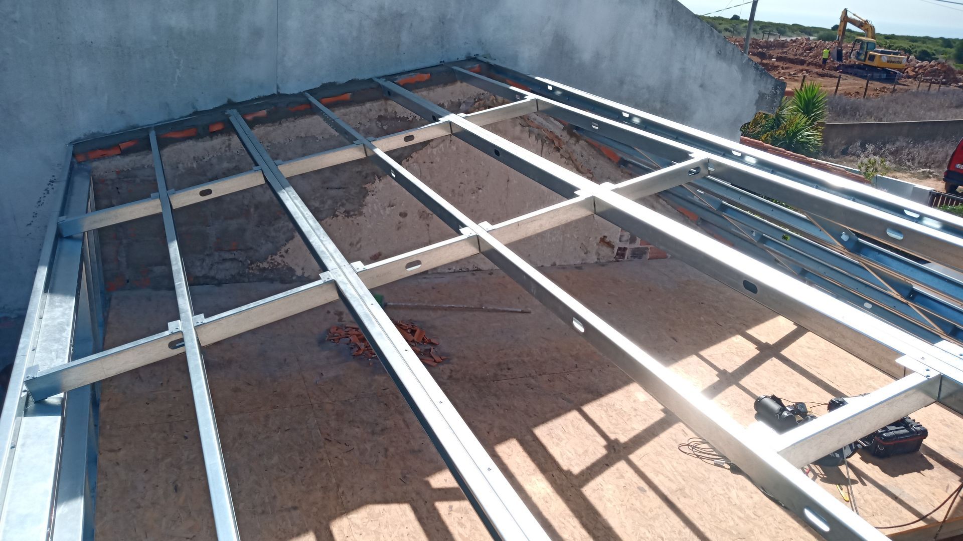 Telhado com estrutura metálica em construção sobre base de madeira, encostado a uma parede.