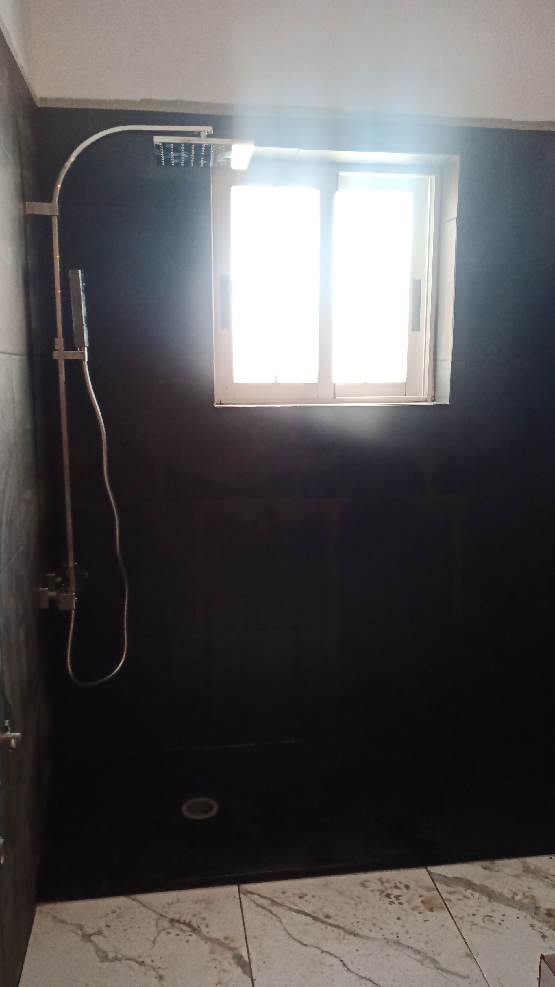 Chuveiro com paredes pretas, acessórios cromados e janela com entrada de luz natural. Piso de mármore.