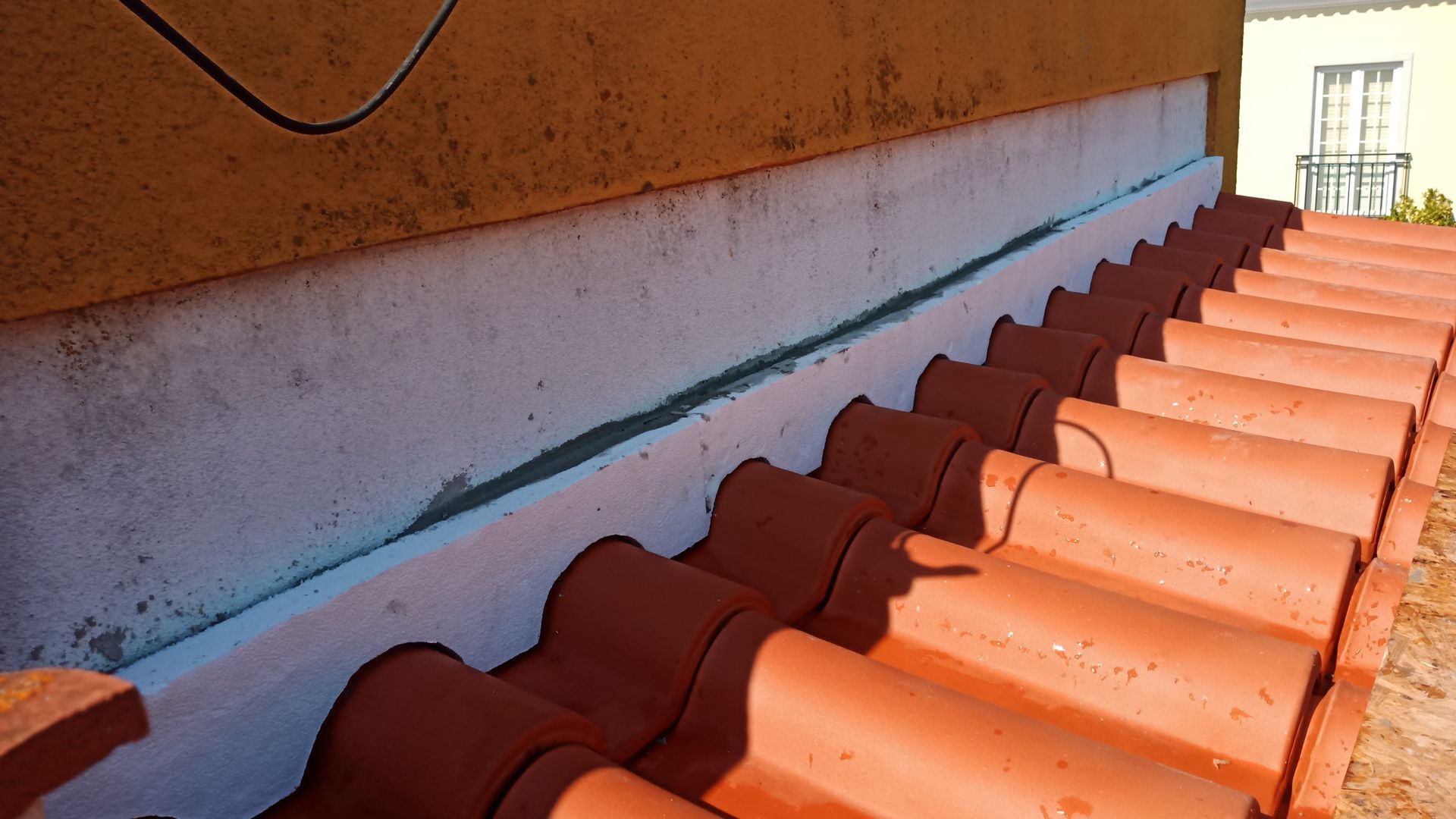 Telhas de barro vermelho contra uma parede branca com emenda. Parede marrom acima.