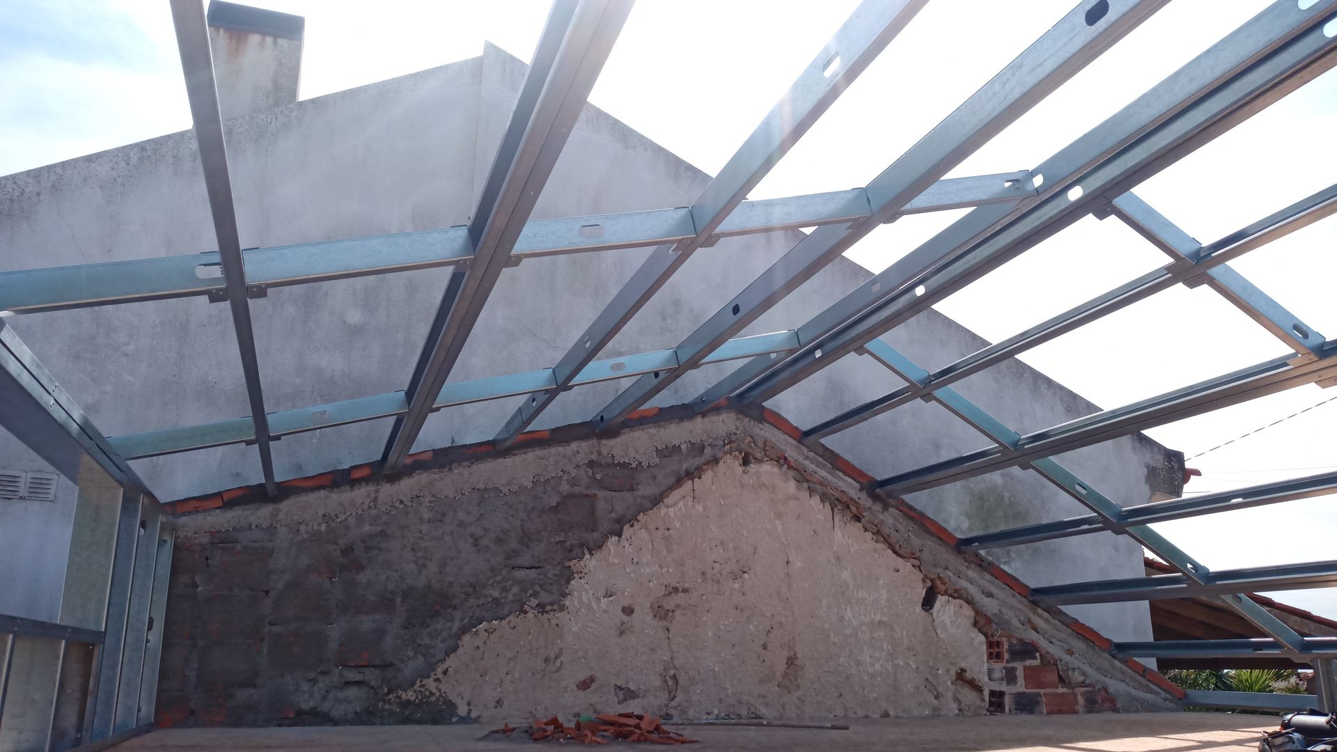 Cobertura com estrutura metálica contrastando com uma parede texturizada de tijolo e concreto.