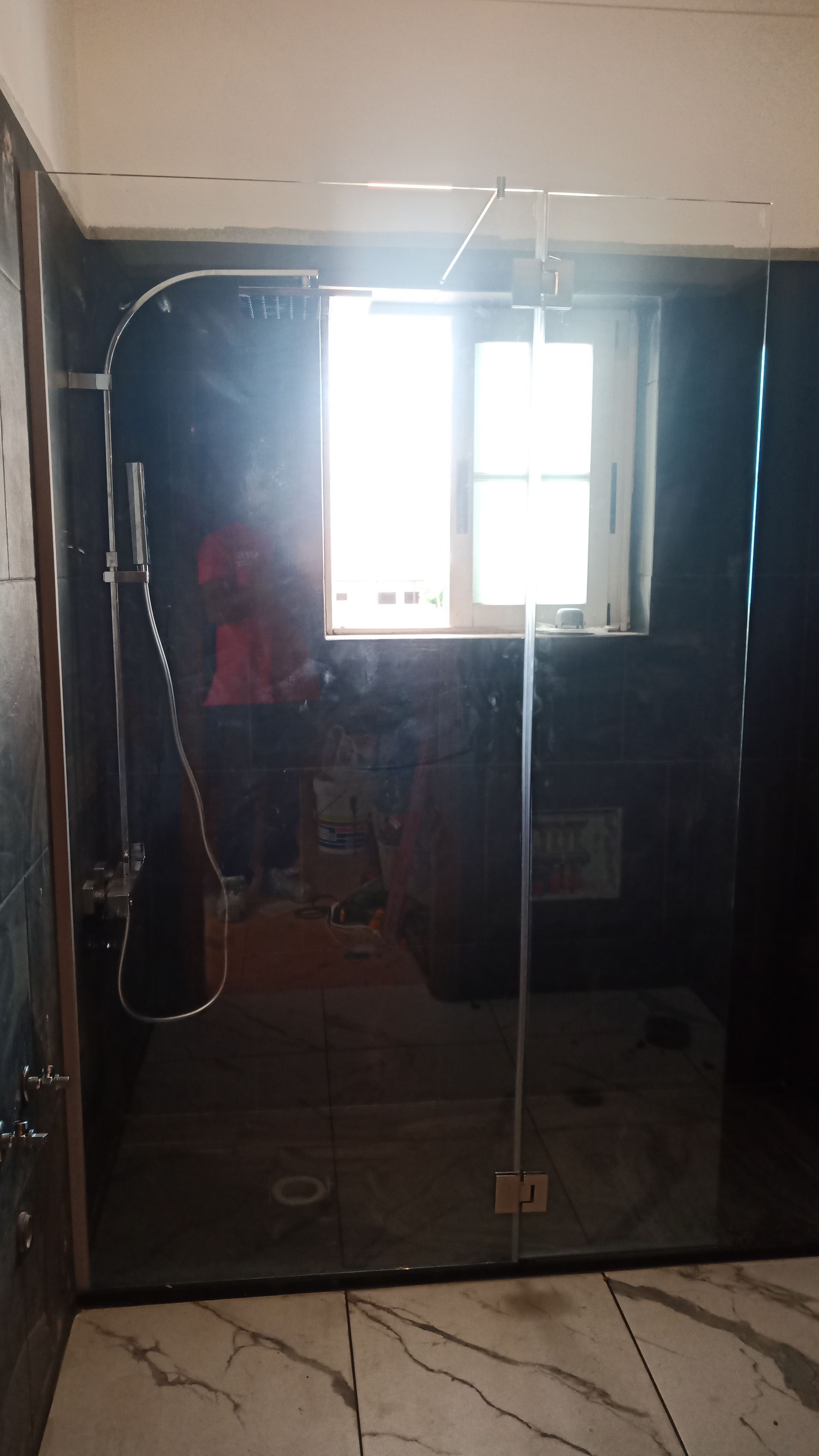 Box de chuveiro com porta de vidro, acessórios prateados, azulejos escuros e janela.