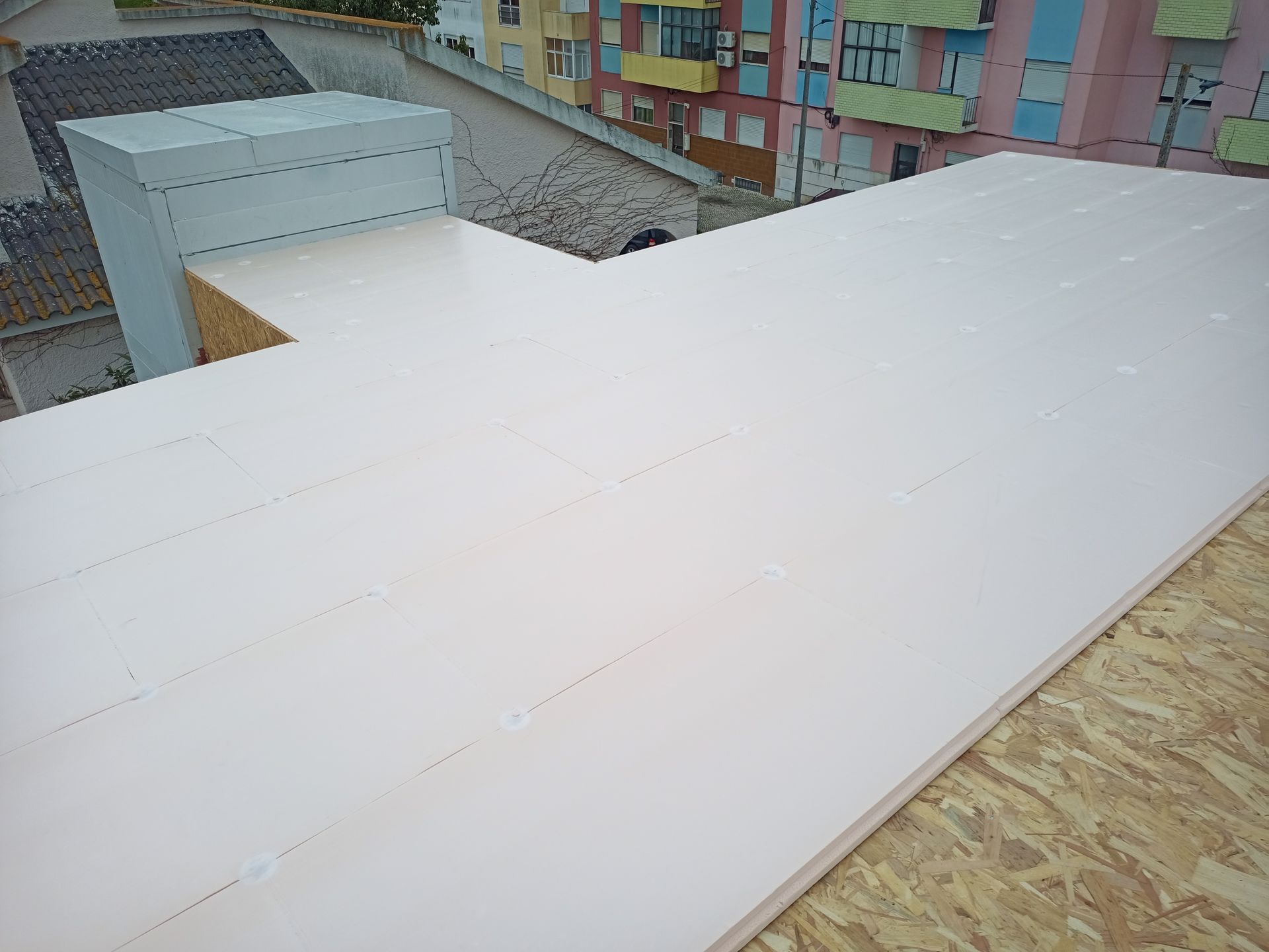 Painéis isolantes rosa no telhado de um edifício, com prédios urbanos ao fundo.