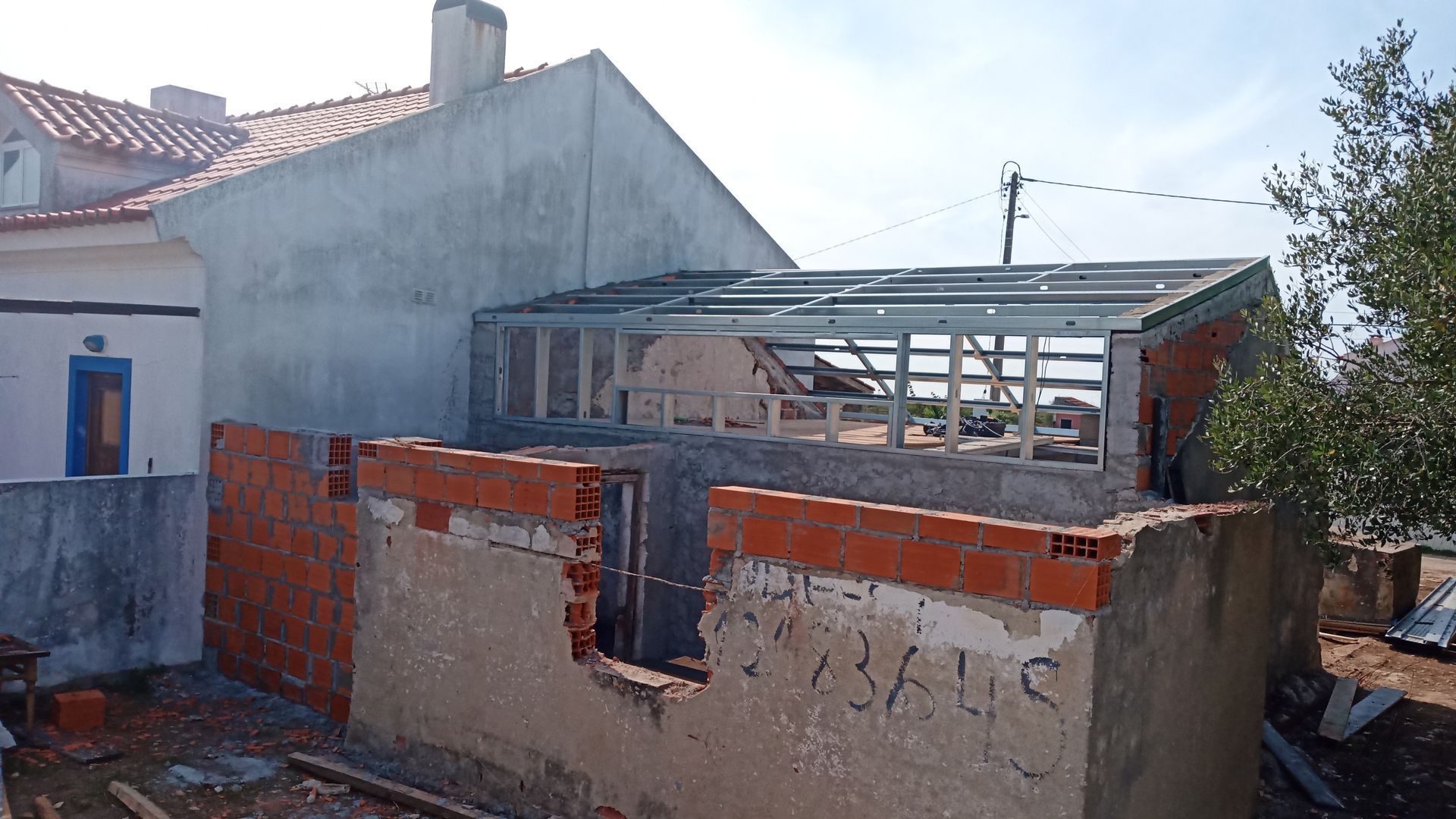 Construção com paredes de tijolo aparente, telhado parcialmente construído e estrutura de concreto cinza.