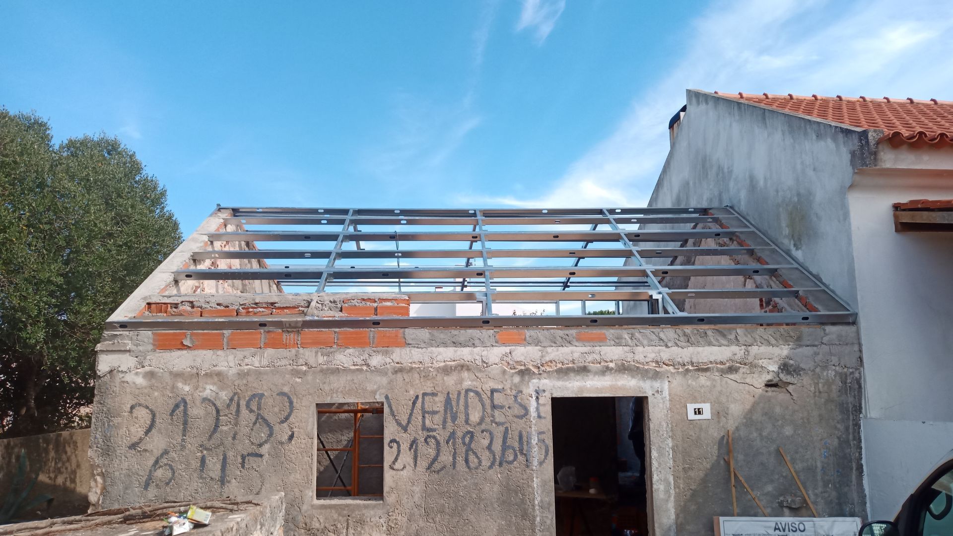 Um prédio parcialmente construído com vigas metálicas no telhado. A palavra 