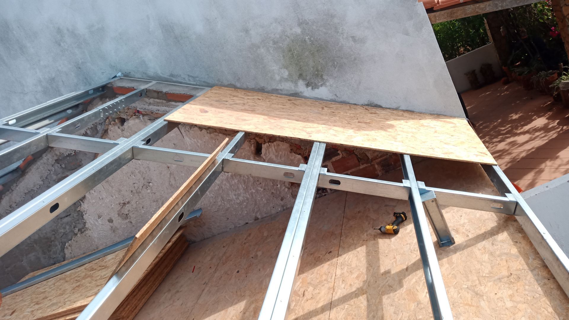 Estrutura metálica com painéis de madeira parcialmente instalados contra uma parede desgastada.