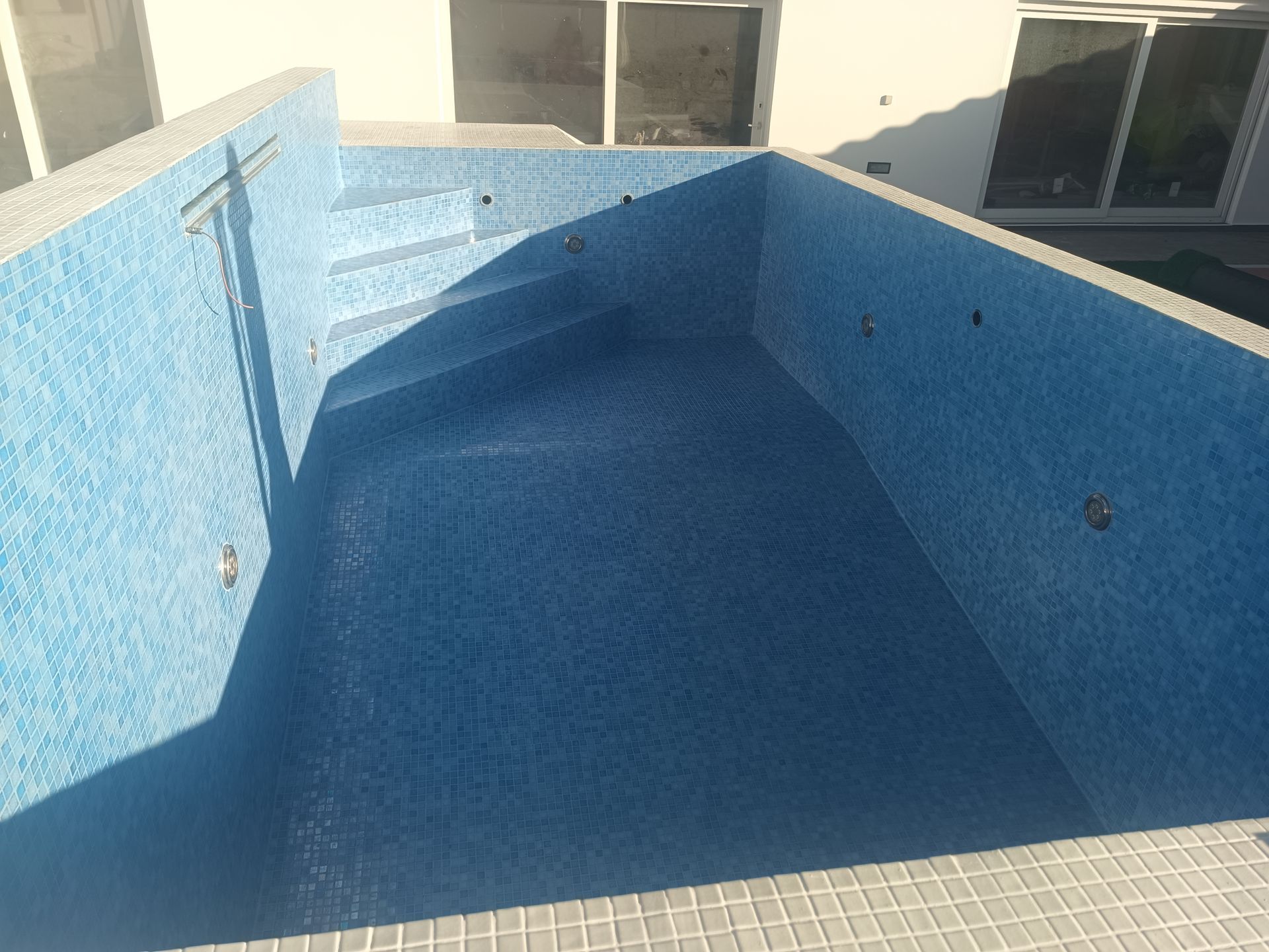 Piscina retangular vazia com interior e degraus revestidos com azulejos azuis, vista de cima.