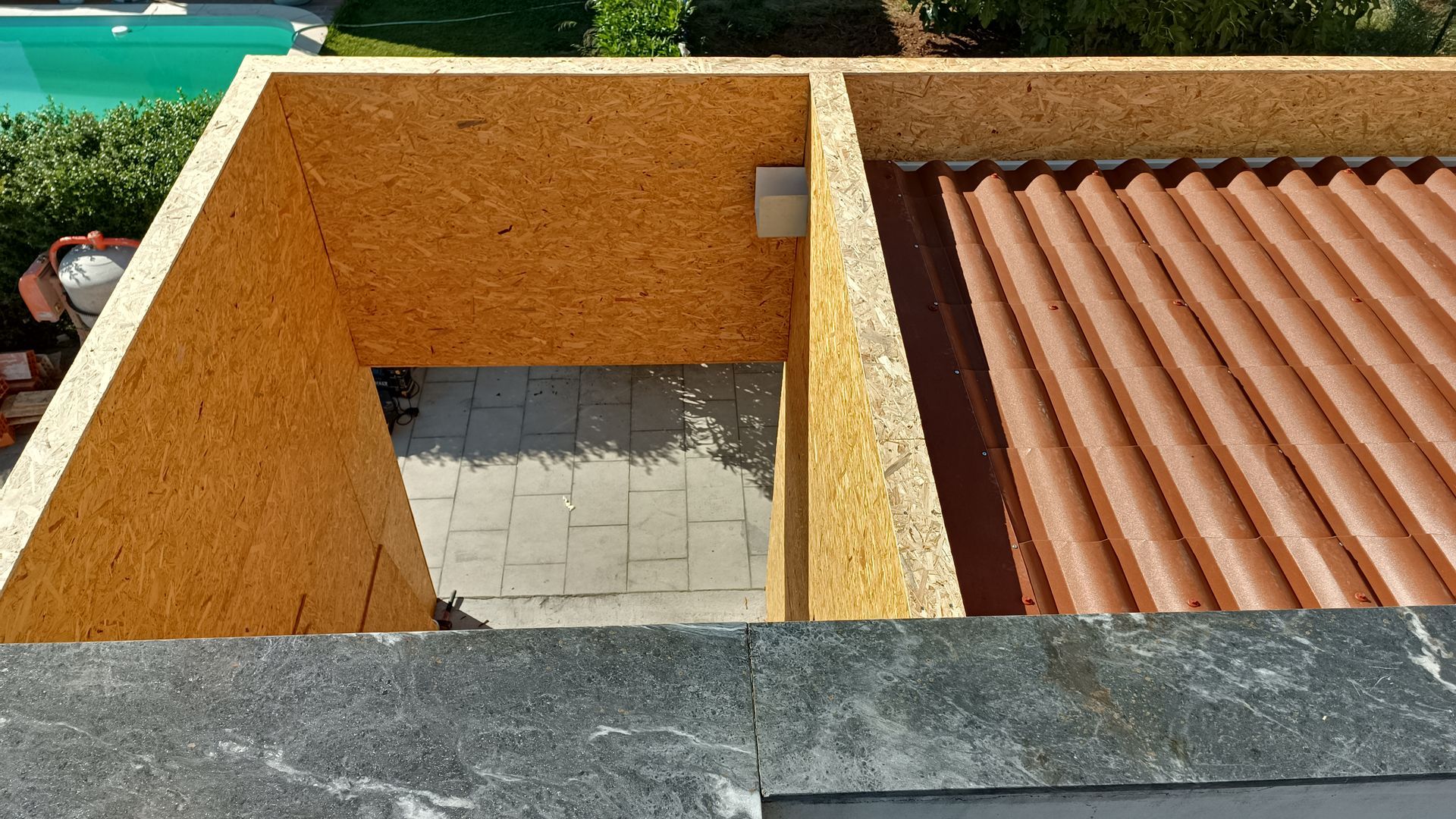 Vista de uma estrutura parcialmente construída com telhado de telha laranja e paredes de OSB.