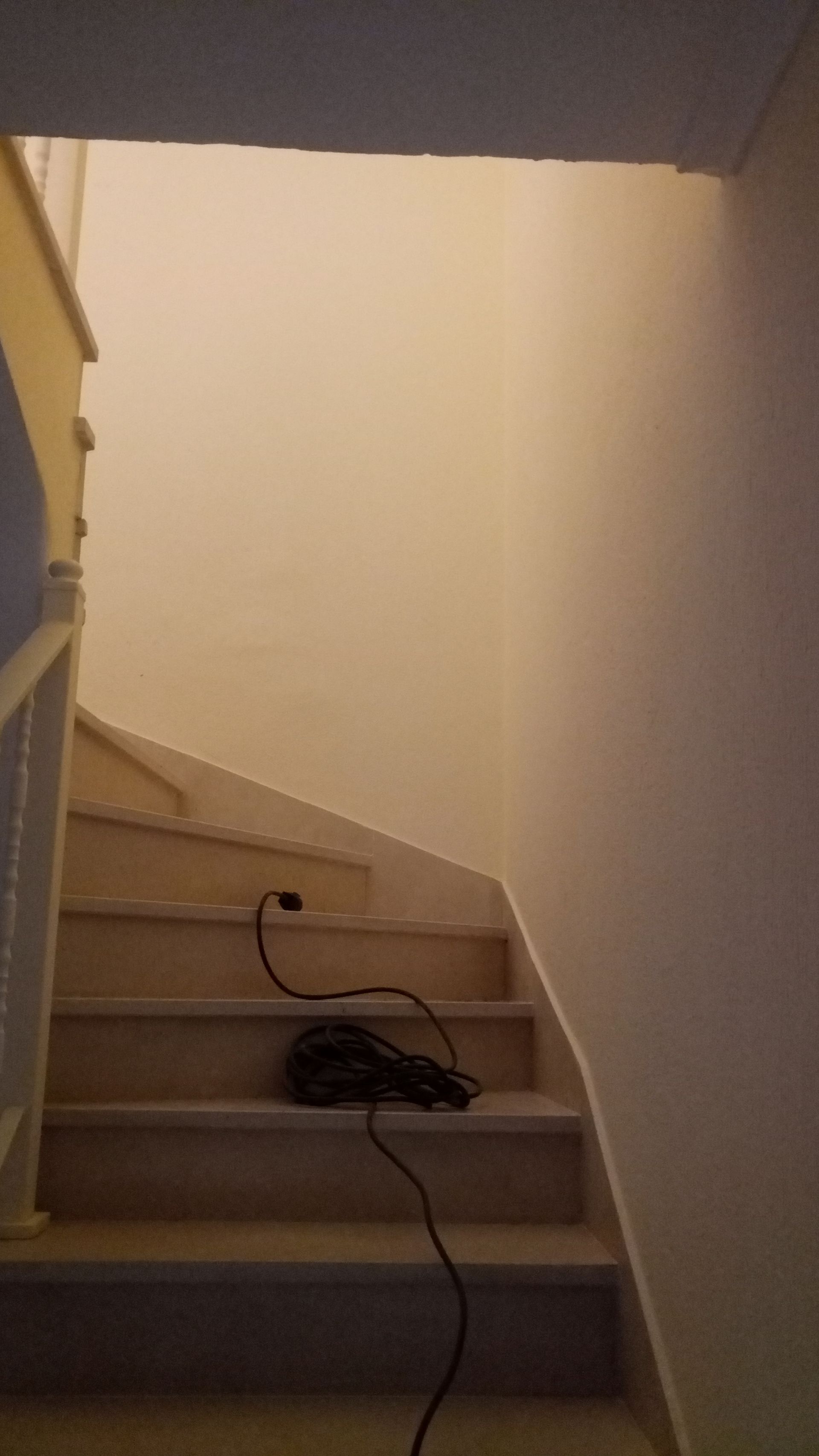 Escada com degraus de madeira e parede branca, com um cabo preto estendido sobre os degraus.