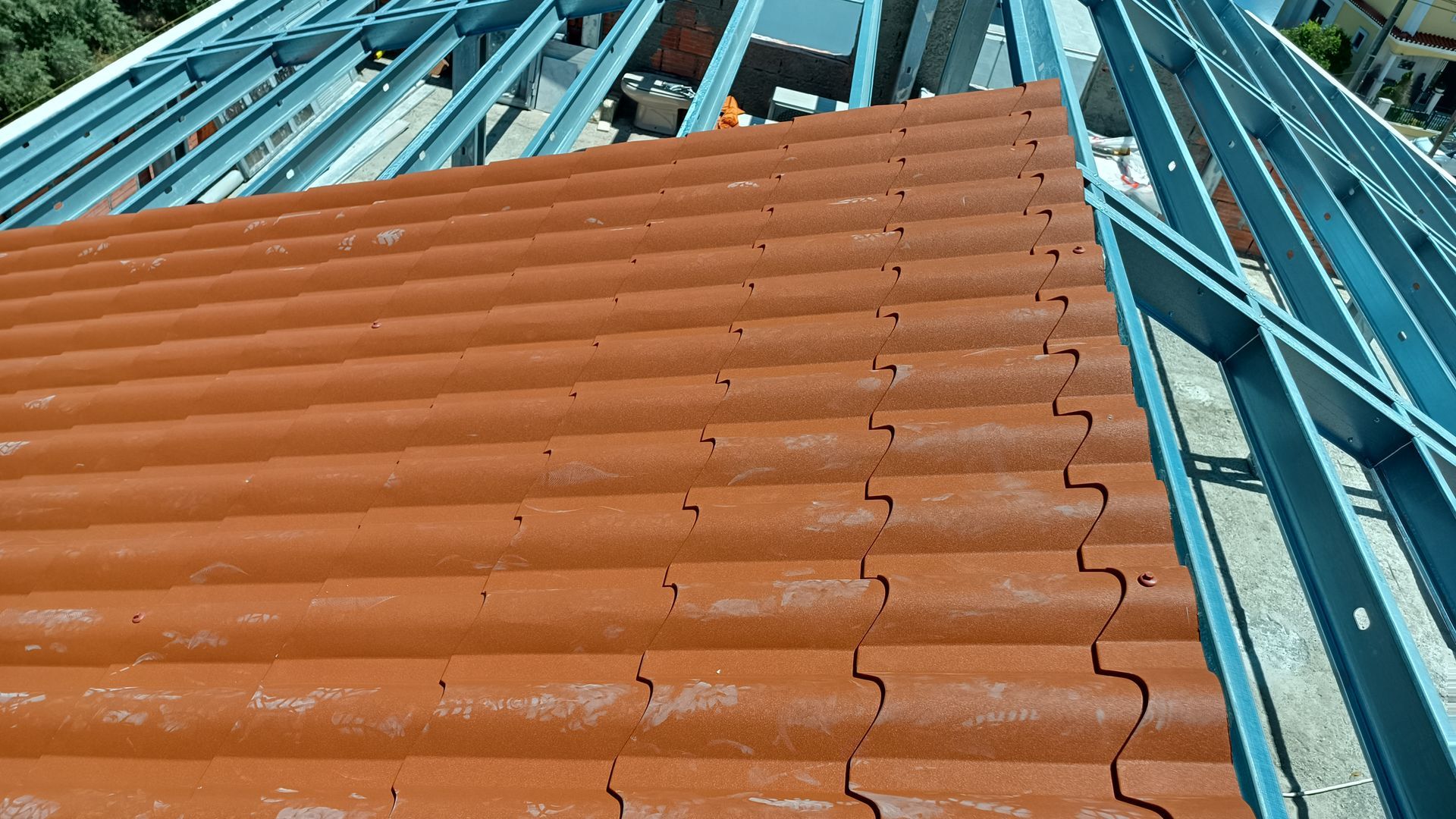 Telhas vermelhas sendo instaladas em uma estrutura metálica, em ambiente externo.
