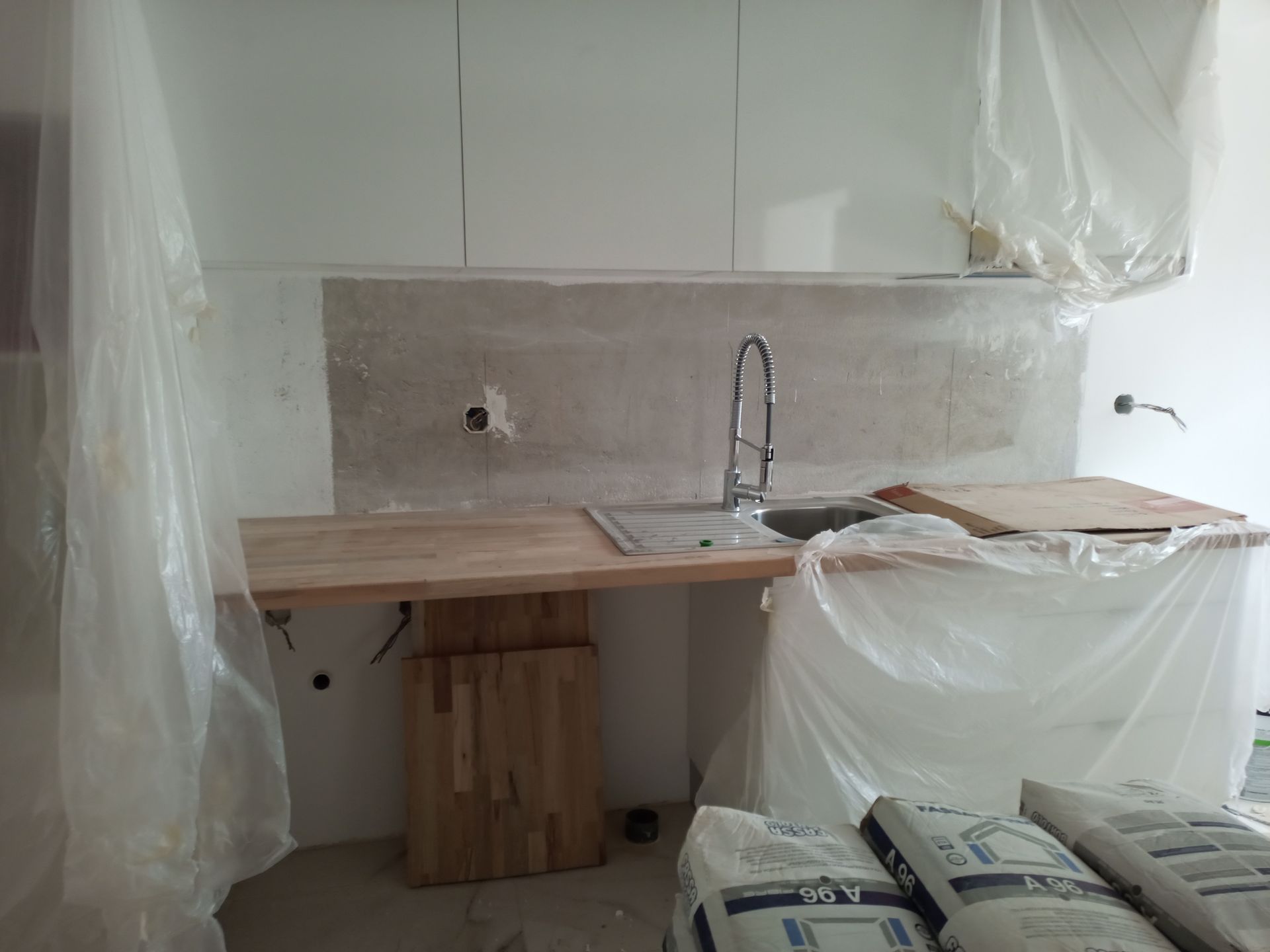 Cozinha em reforma, com pia, bancada, armários e lona plástica.