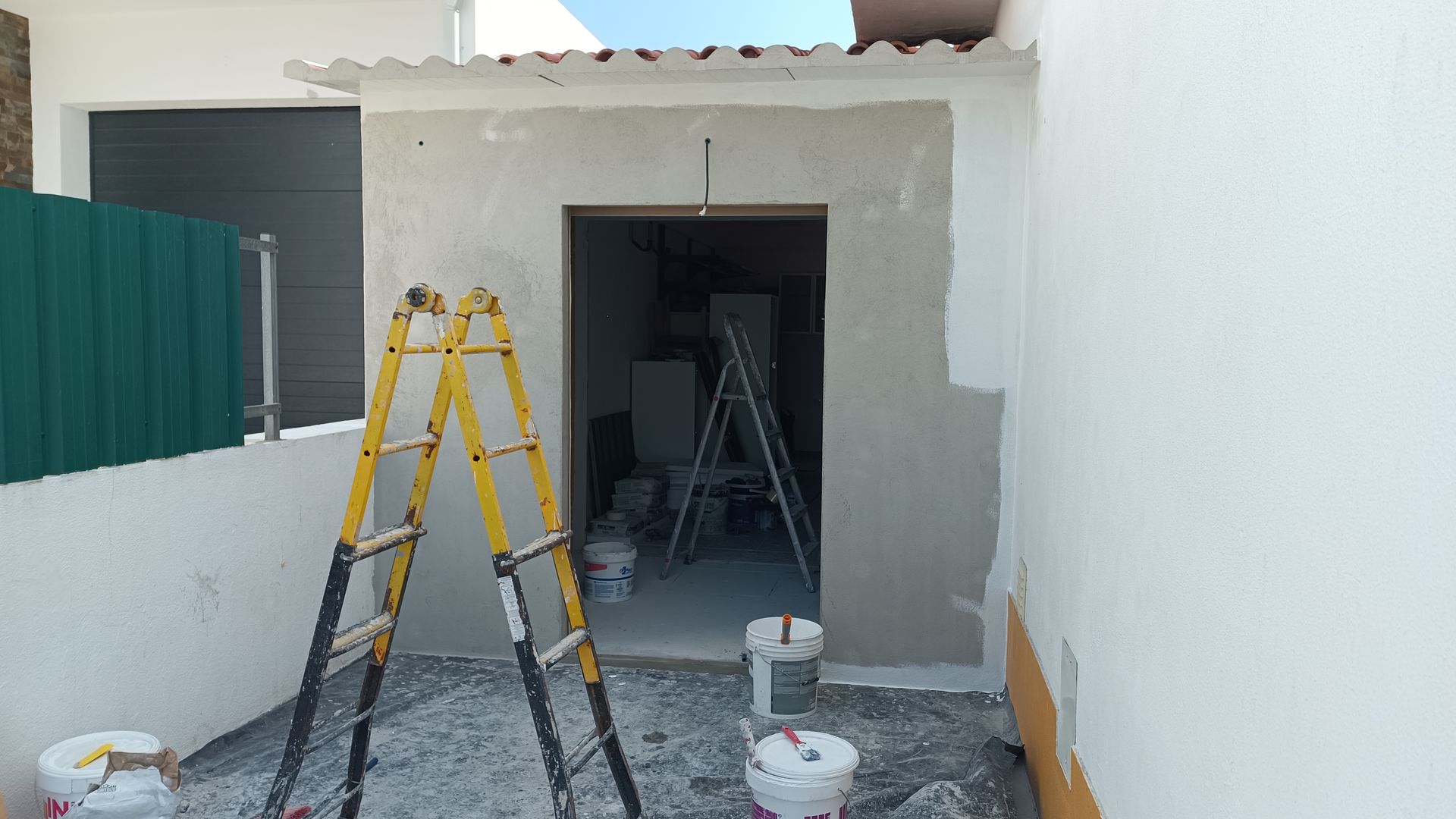 Canteiro de obras: porta com escada amarela, paredes inacabadas, baldes de tinta e ferramentas.