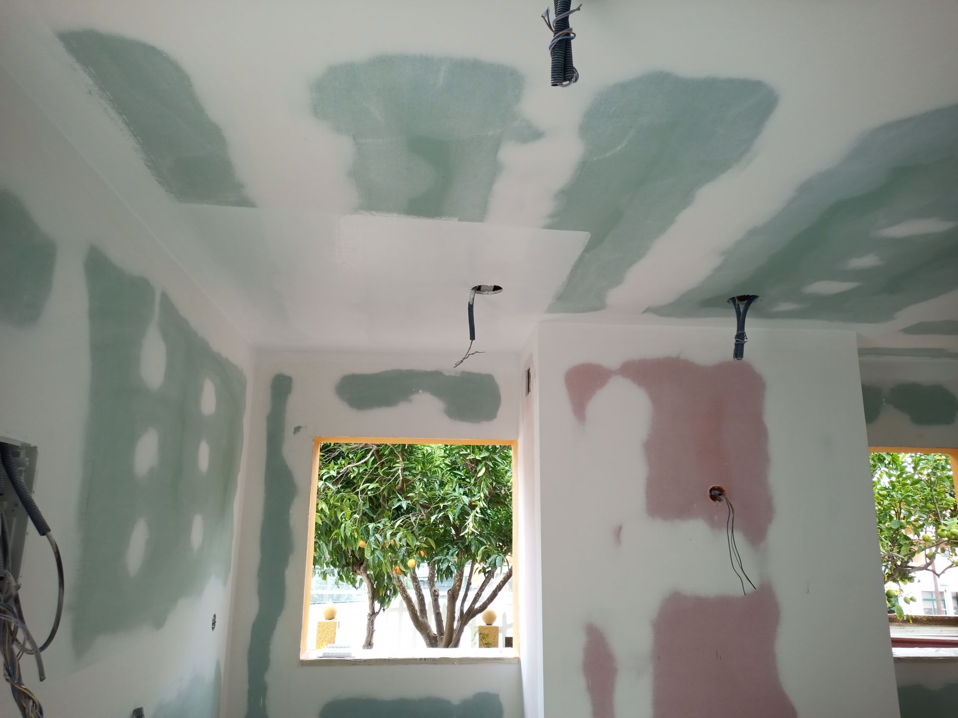 Vista interna de um cômodo em construção com remendos de gesso cartonado verde e rosa nas paredes e no teto.