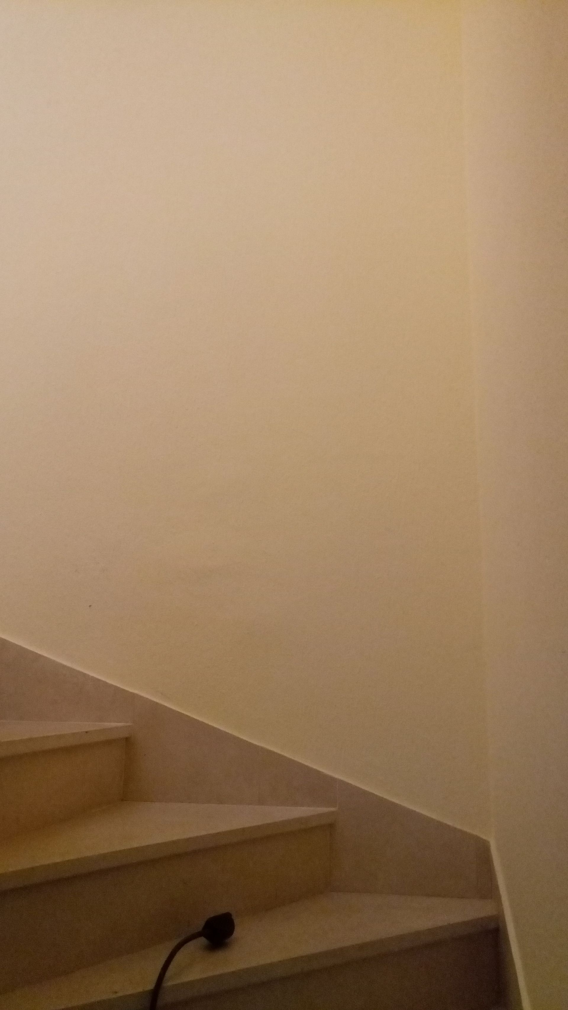 Escada com degraus bege claro e parede bege; um fio preto está no degrau inferior.