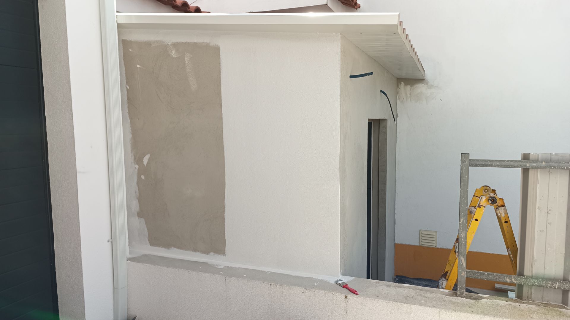 Parede exterior em construção com seção parcialmente rebocada e escada.