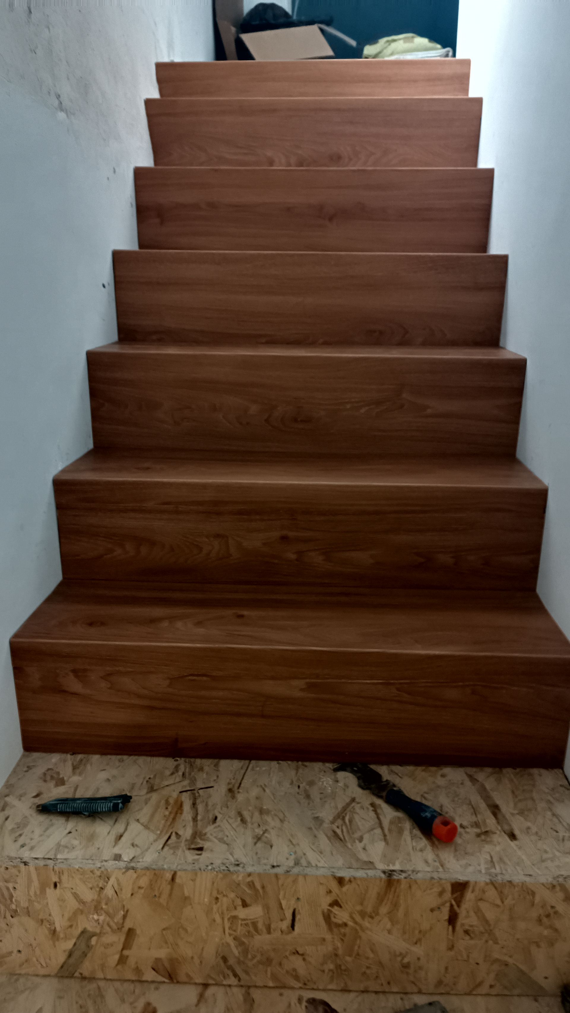 Escada de madeira recém-instalada que leva ao andar superior. Ferramentas de carpinteiro estão no degrau inferior.