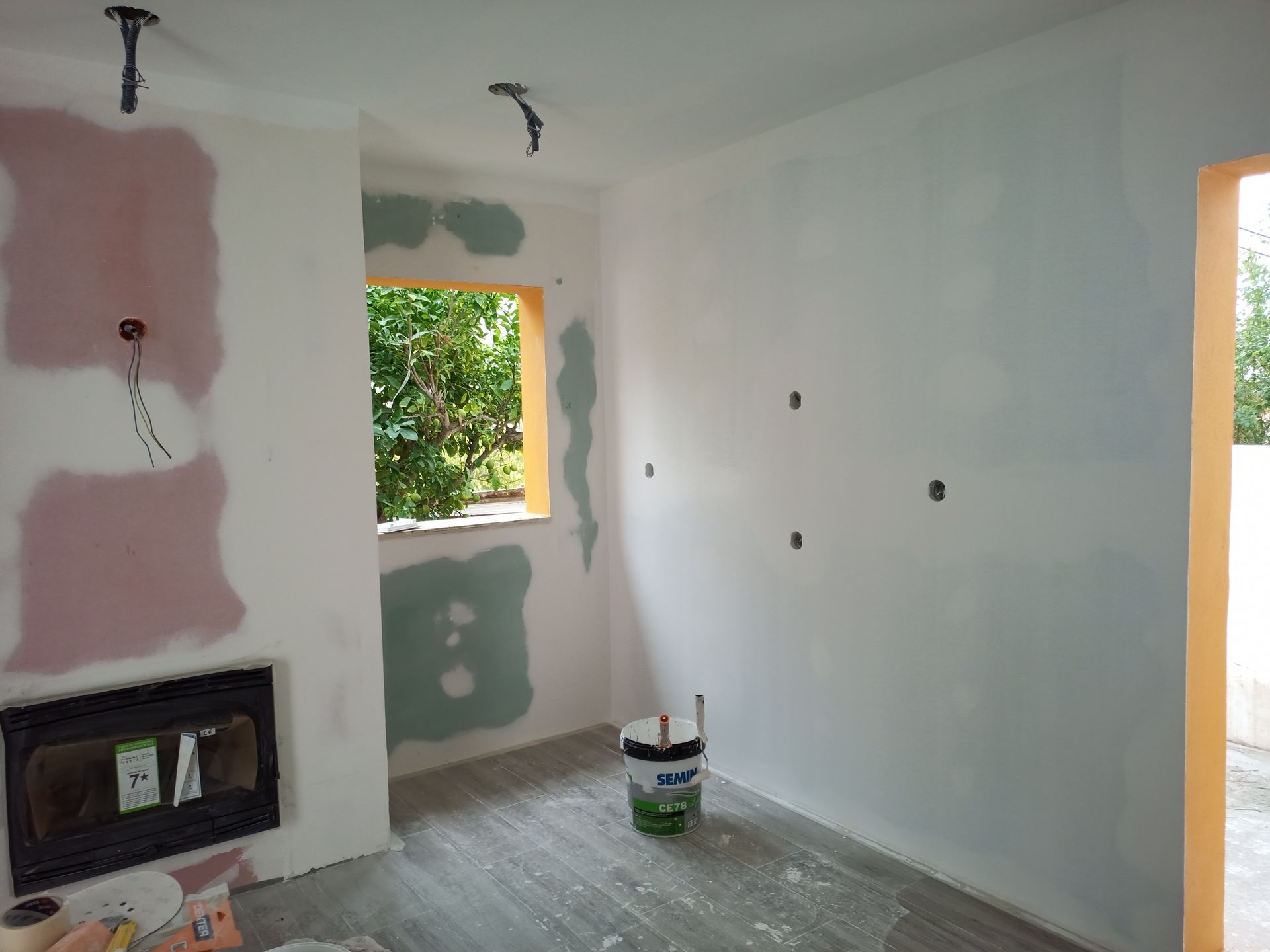 Cômodo interno em construção, com drywall aparente, janela e lareira inacabada.
