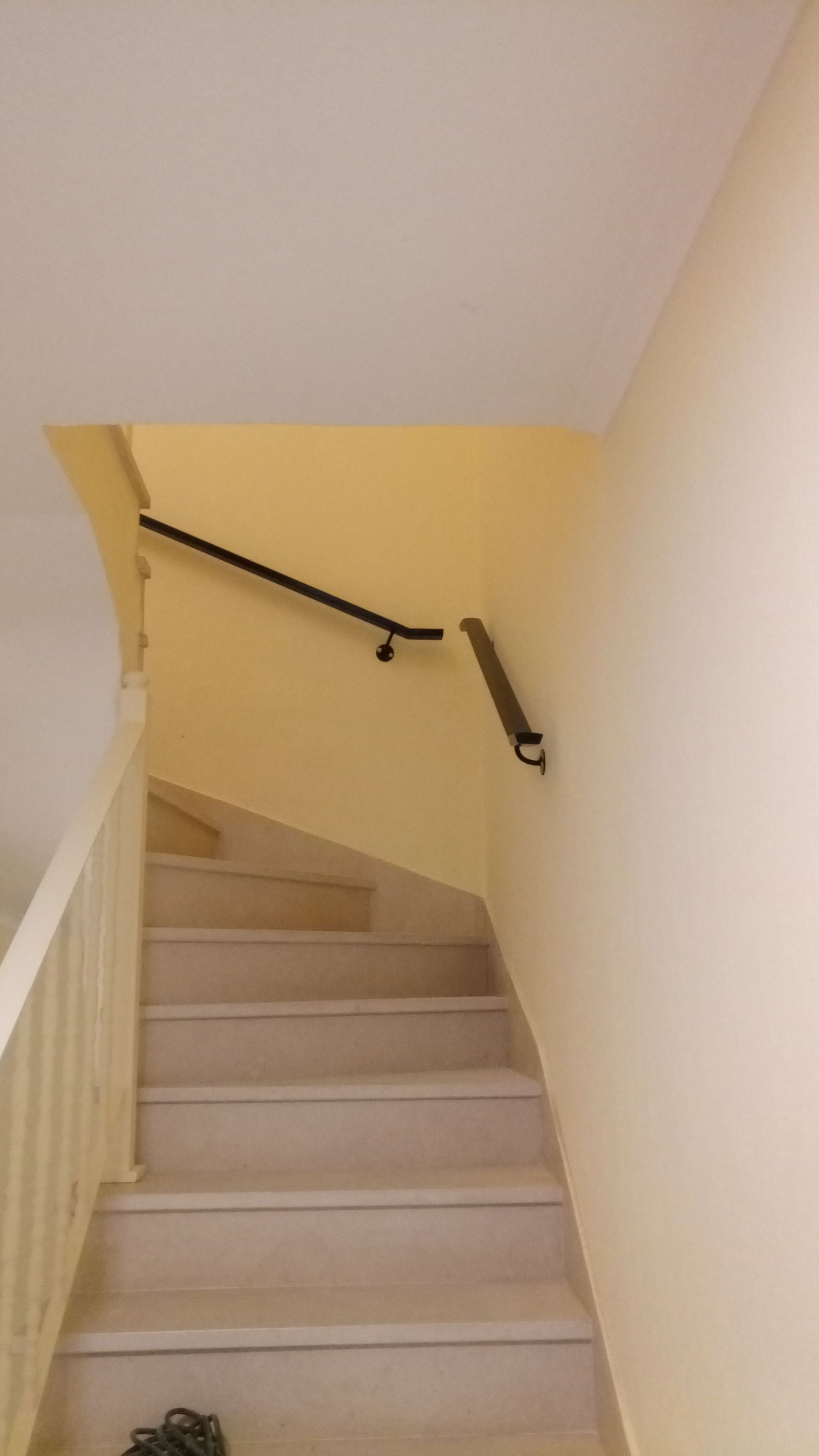 Escadaria com degraus de pedra clara, paredes amarelas e corrimão preto.